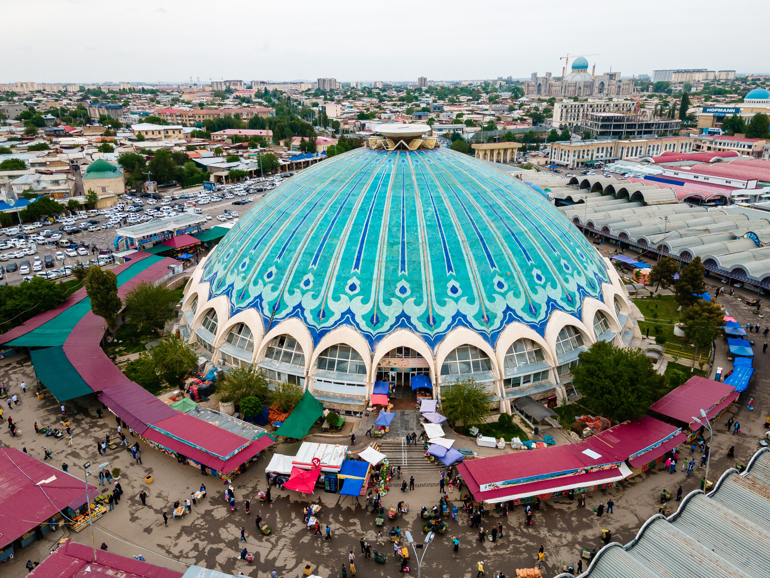Aerial view of a large turquoise-domed market hall with a blue patterned roof, surrounded by stalls and city streets.