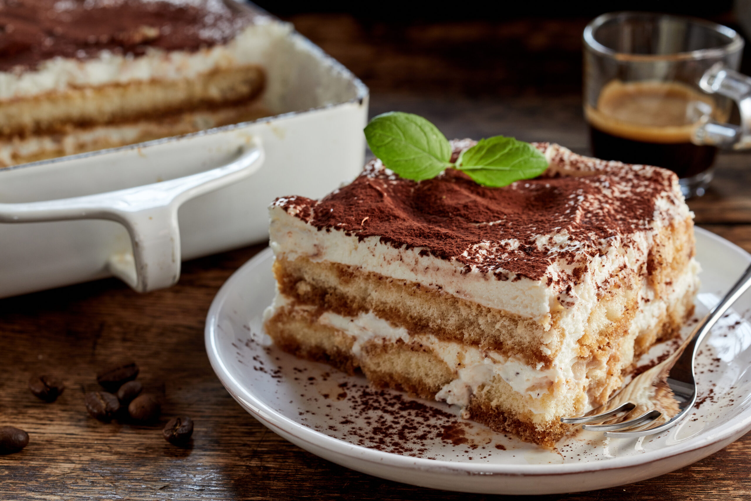 Two slices of tiramisu on a white plate with cocoa powder and a mint leaf garnish.