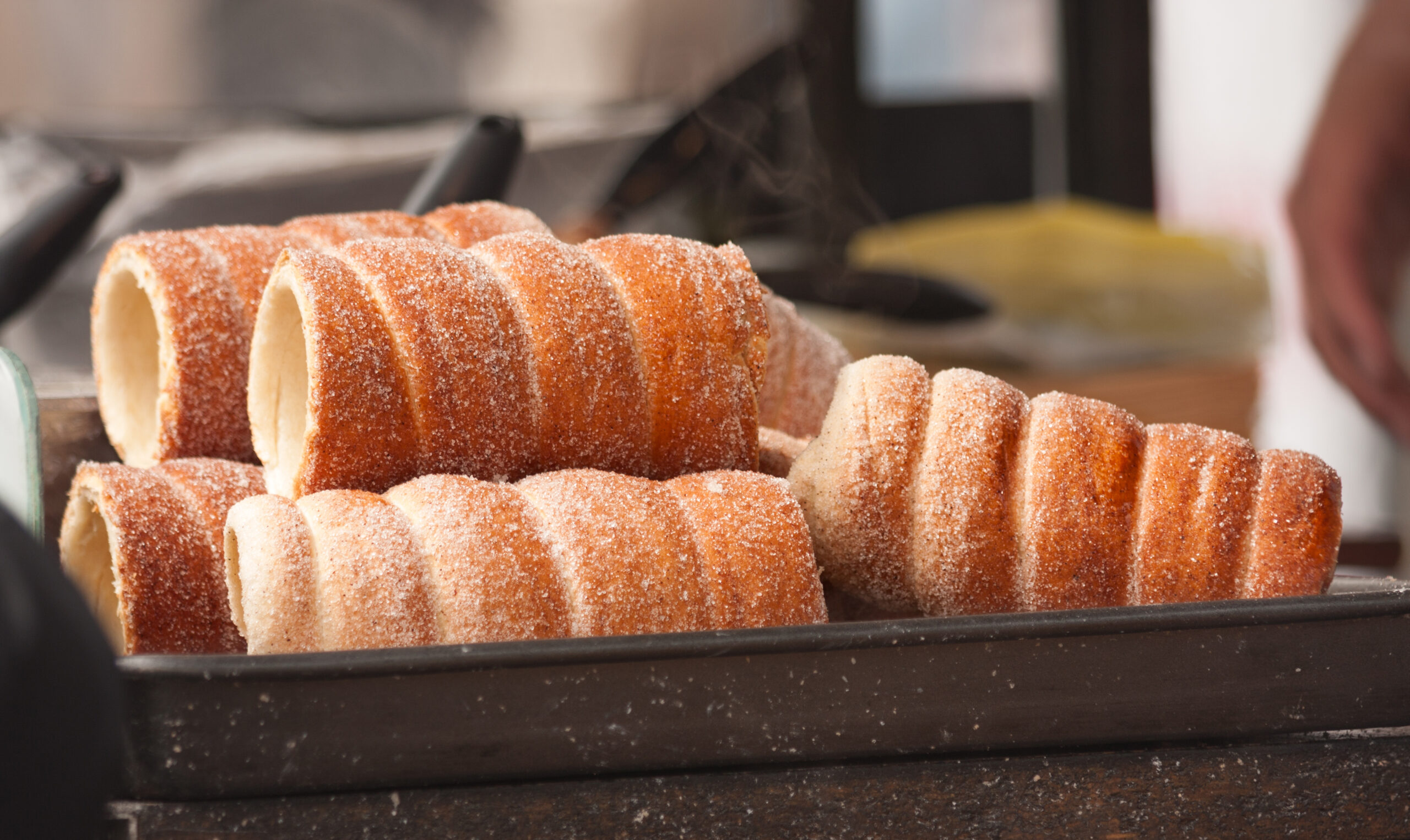 Stacks of sugar-dusted ring-shaped pastries in a bakery display case on a dark tray