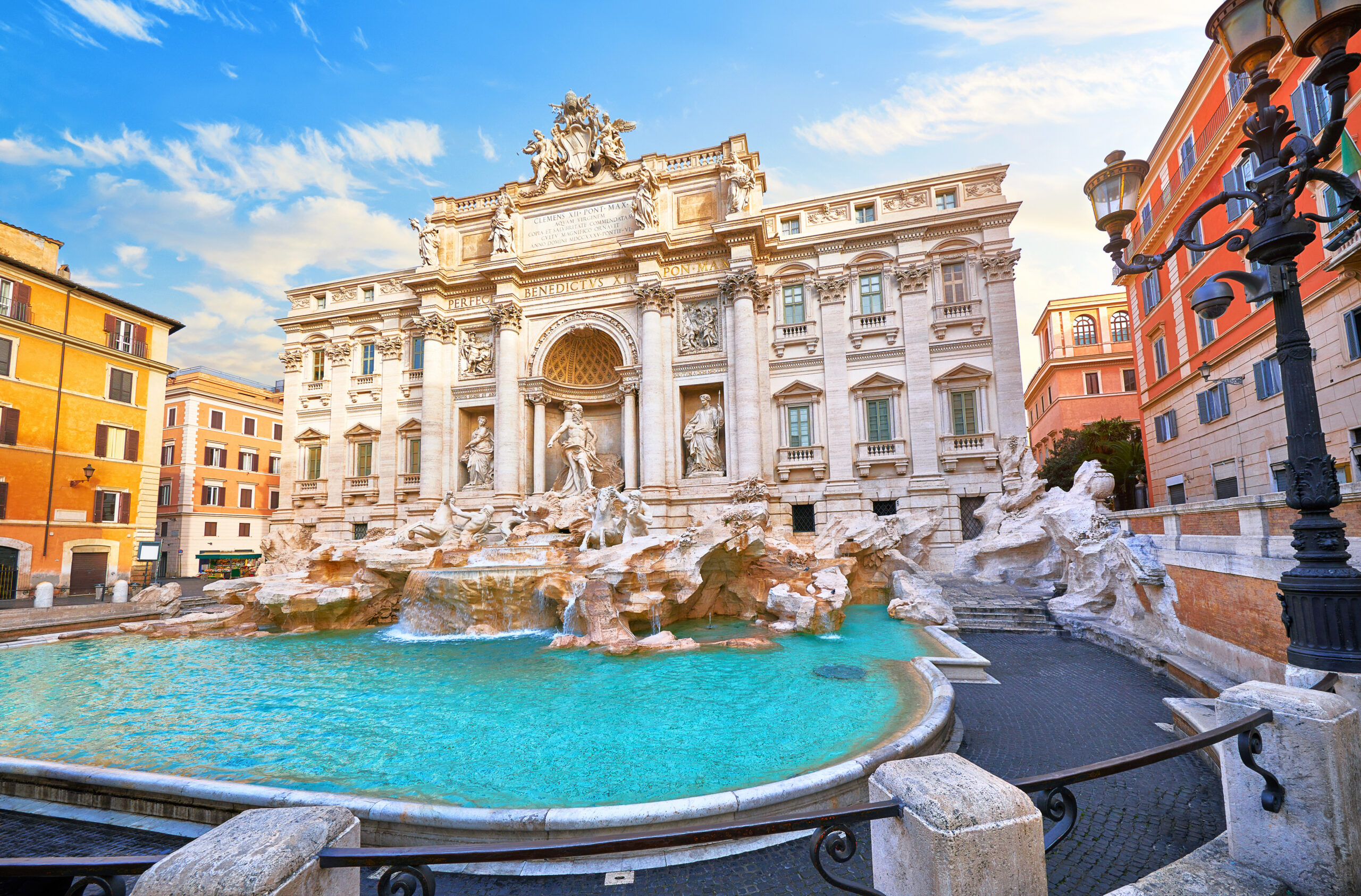 Trevi Fountain in Rome with statues, central arch, and turquoise pool framed by orange buildings while a bright sky shines above.