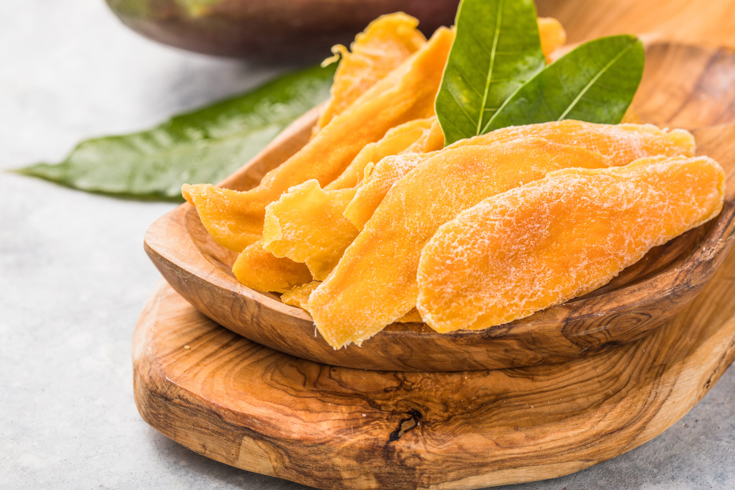 Dried mango slices on a wooden board with green leaves in the background