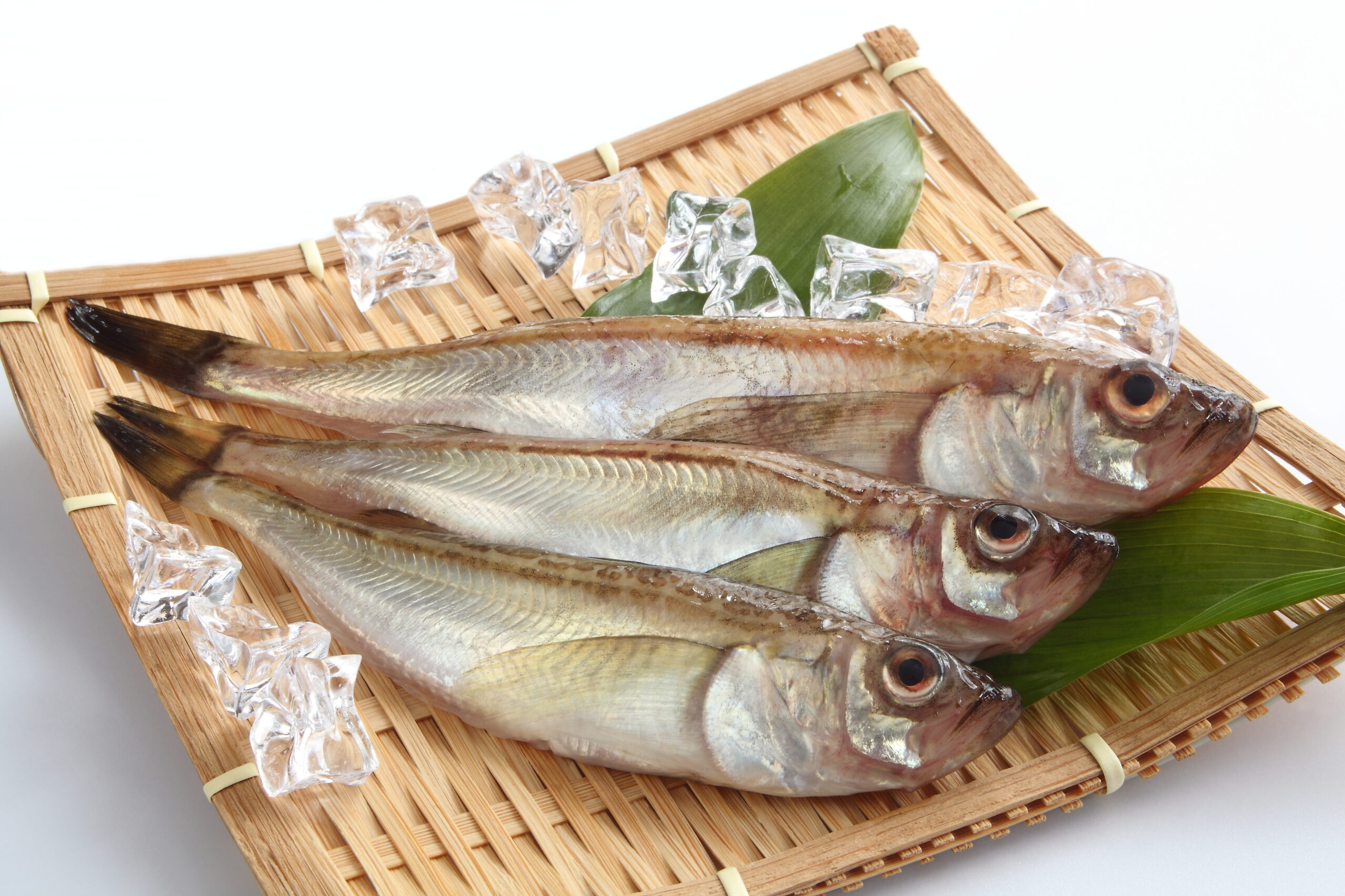 Fresh whole fish laid on a bamboo tray with ice cubes and a green leaf garnish.