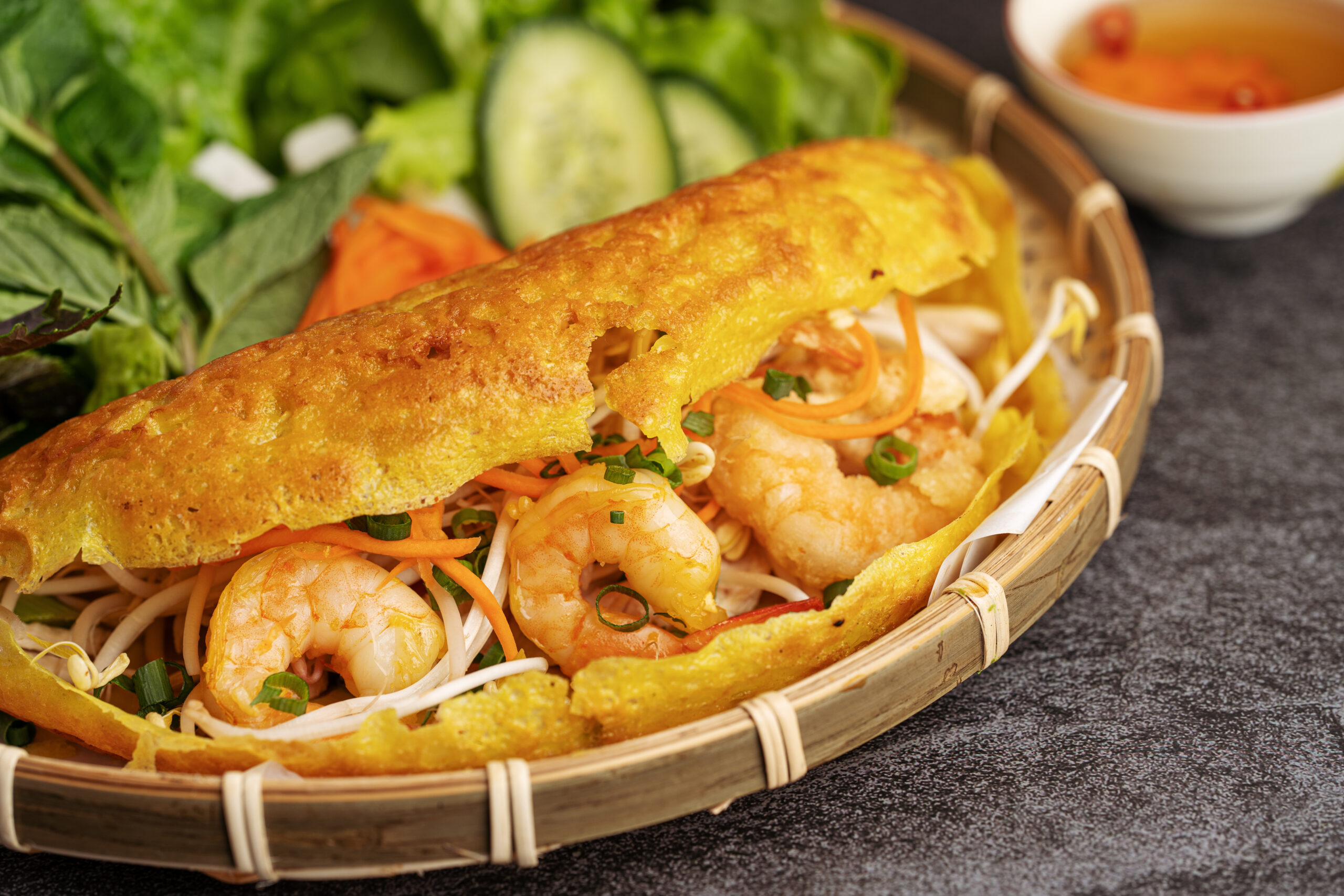 Basket of fresh spring rolls with shrimp, vermicelli, and herbs, in a woven basket on a dark surface.