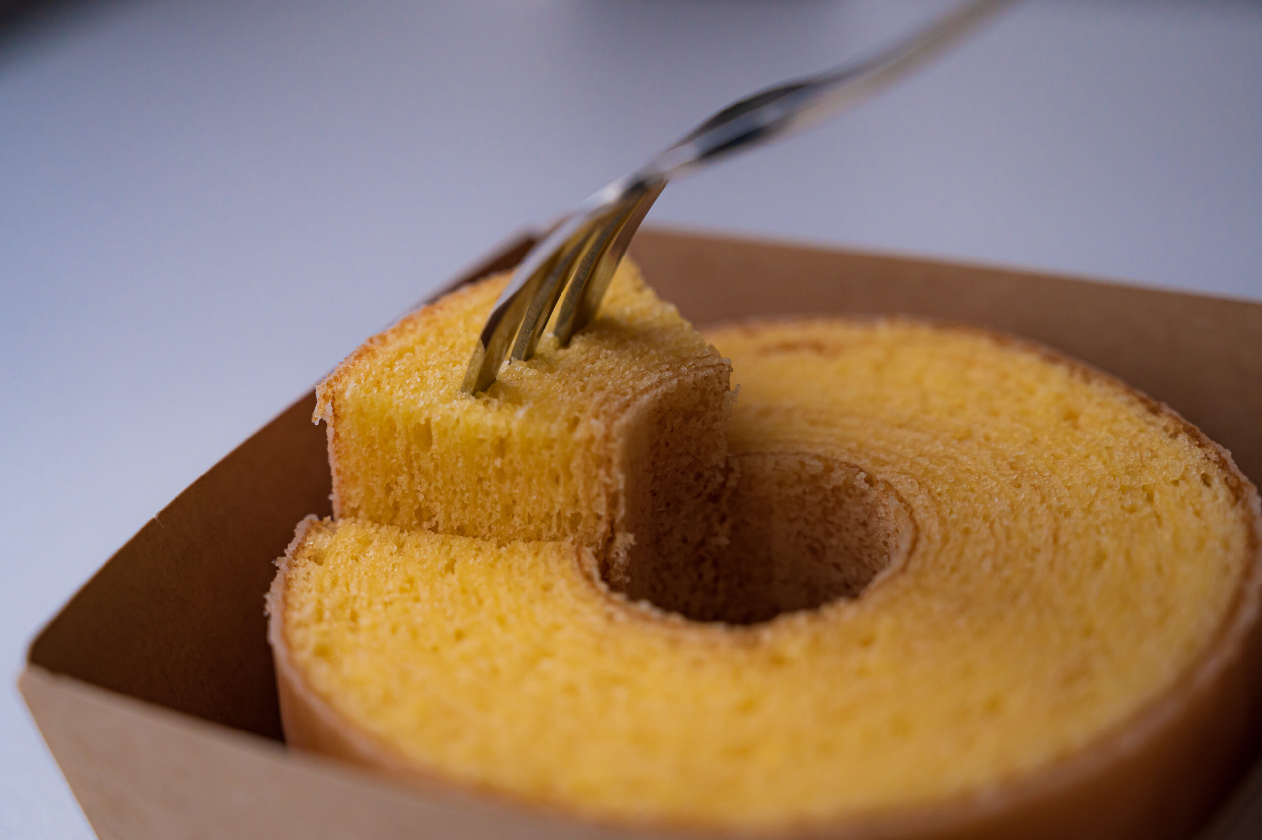 Slices of golden pound cake arranged in a cardboard box, with a fork stabbing a piece of cake.