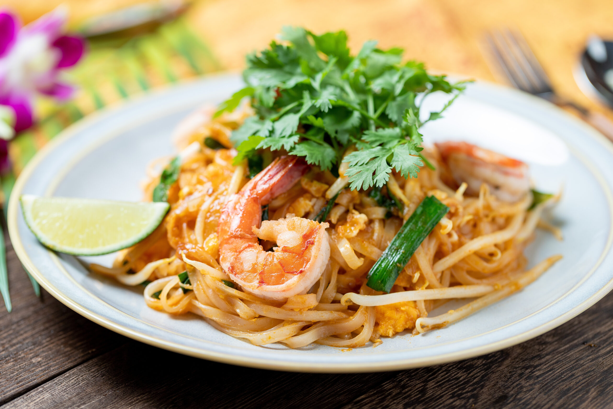 Plate of shrimp pasta garnished with cilantro and lime wedges on a blue-rimmed plate