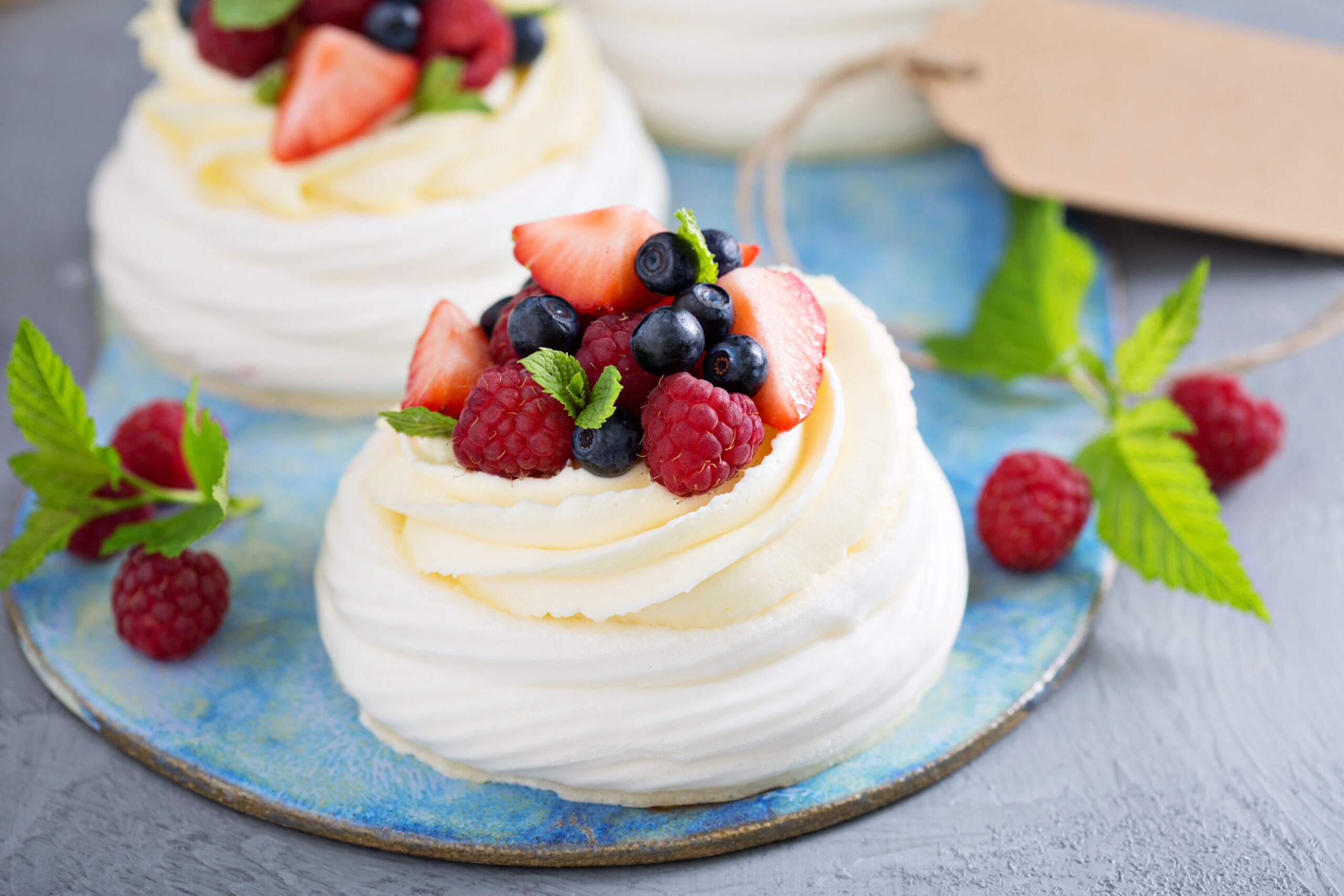Cupcake with white frosting topped with strawberries, blueberries, raspberries and mint on a blue plate.