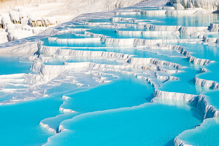 White travertine terraces filled with bright blue mineral-rich water forming cascading pools
