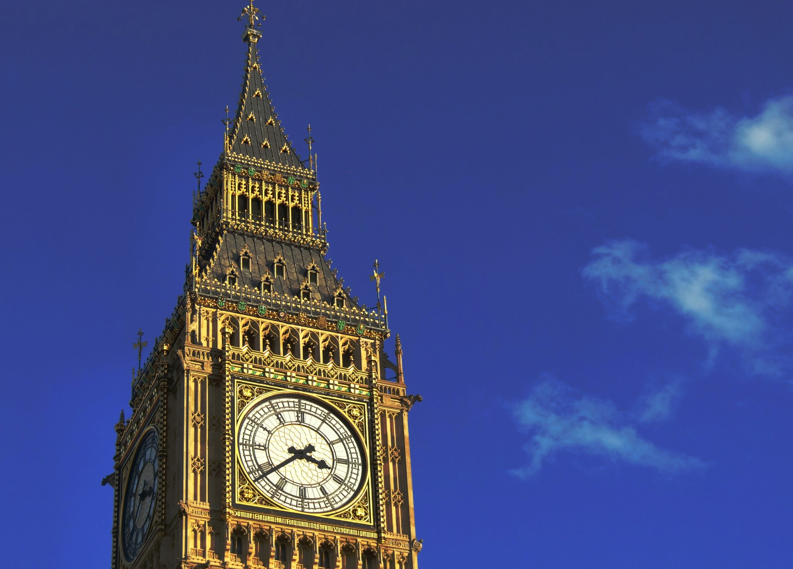 Elizabeth Tower (Big Ben) clock tower rising against a clear blue sky, with ornate Gothic detailing visible around the clock face.
