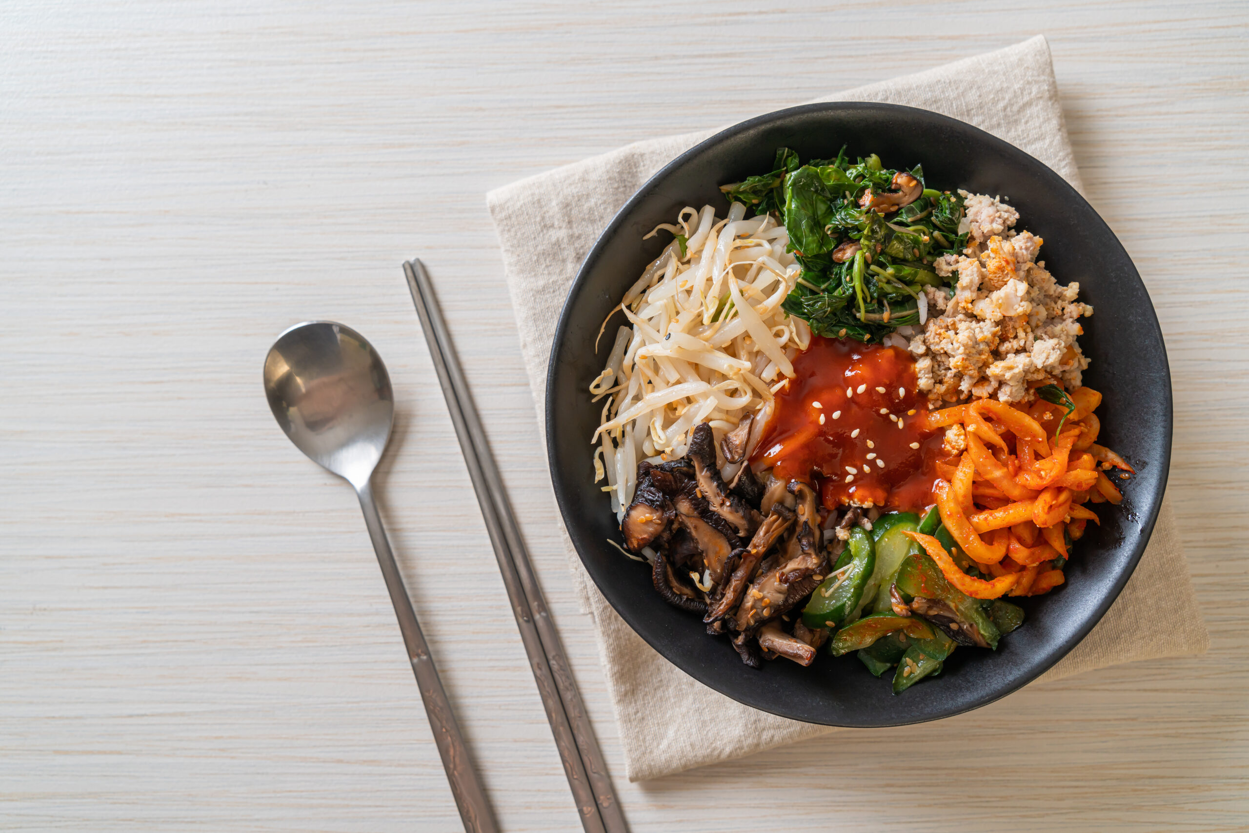 Bowl of bibimbap with rice noodles, greens, minced meat, and gochujang red sauce, sesame seeds on top.