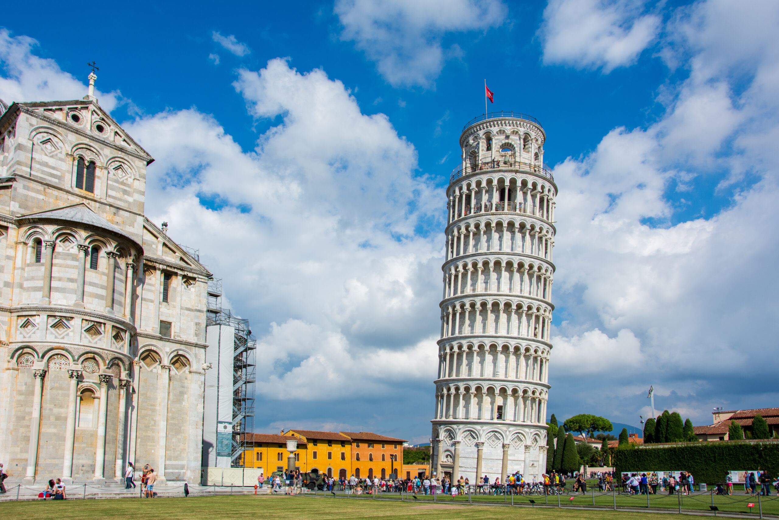 Leaning Tower of Pisa beside the cathedral with tourists in a sunlit plaza under a blue sky.