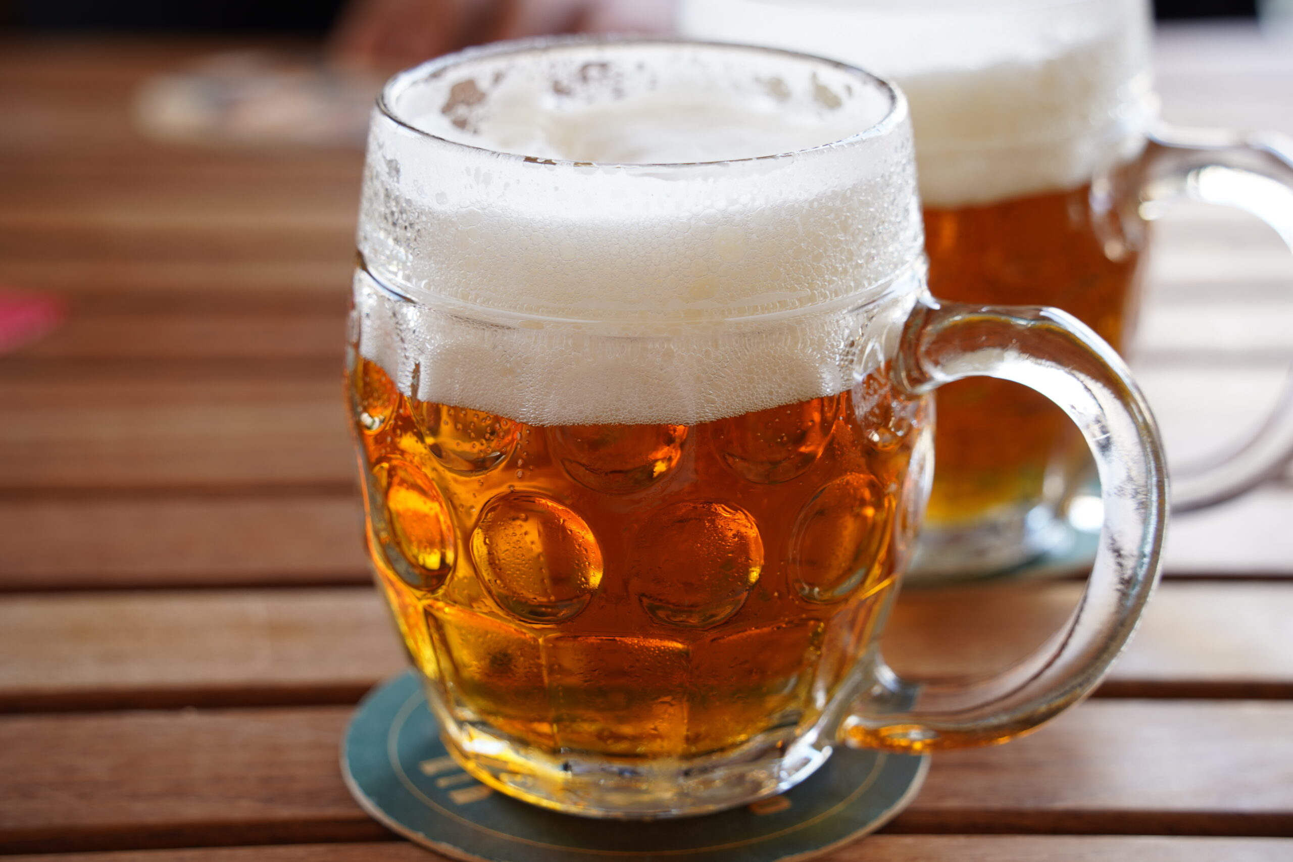 Glass beer mug filled with amber beer and a foamy white head on a wooden table.