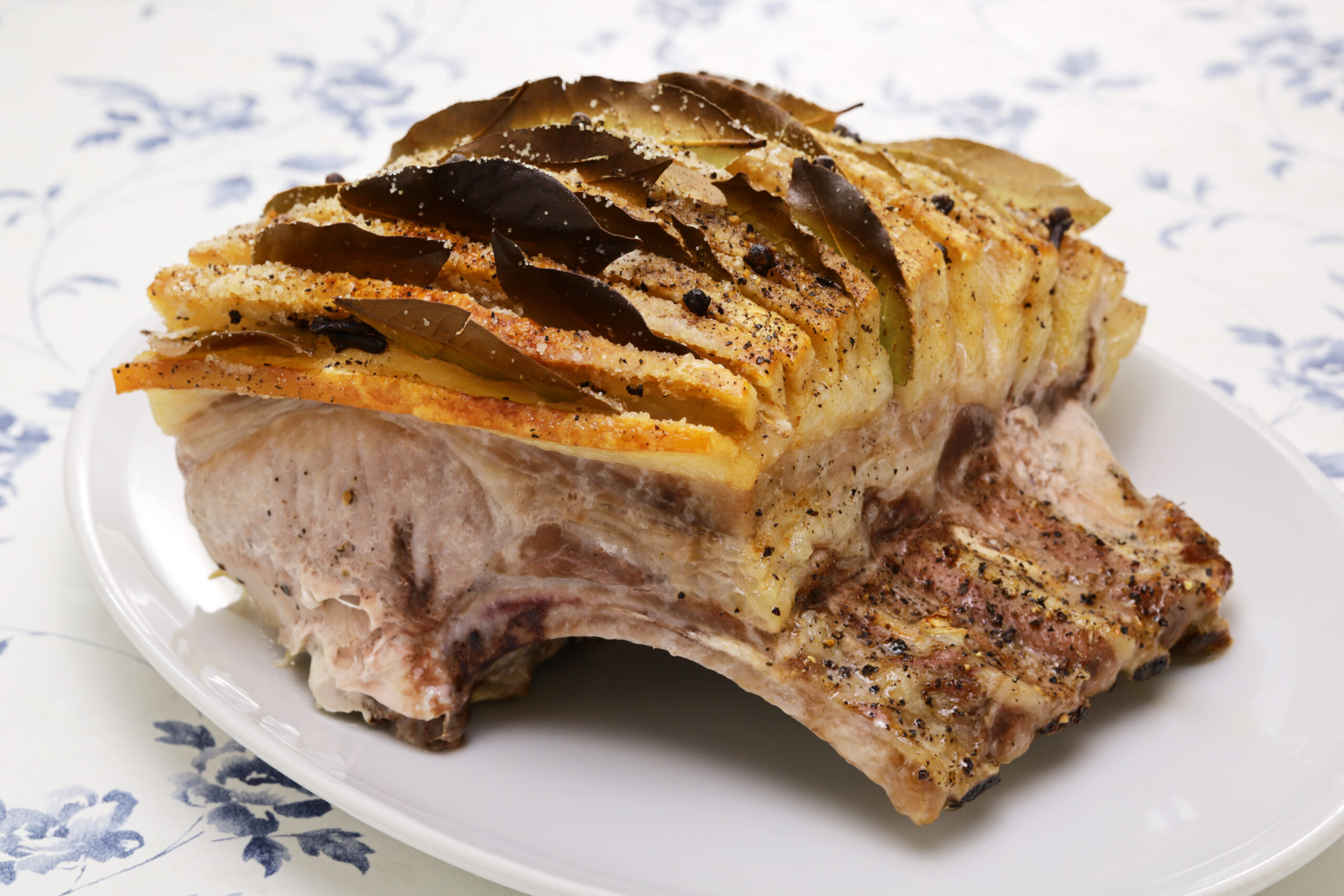 Roast chicken leg on a white plate topped with crispy potato slices and herbs, sprinkled with pepper and salt.