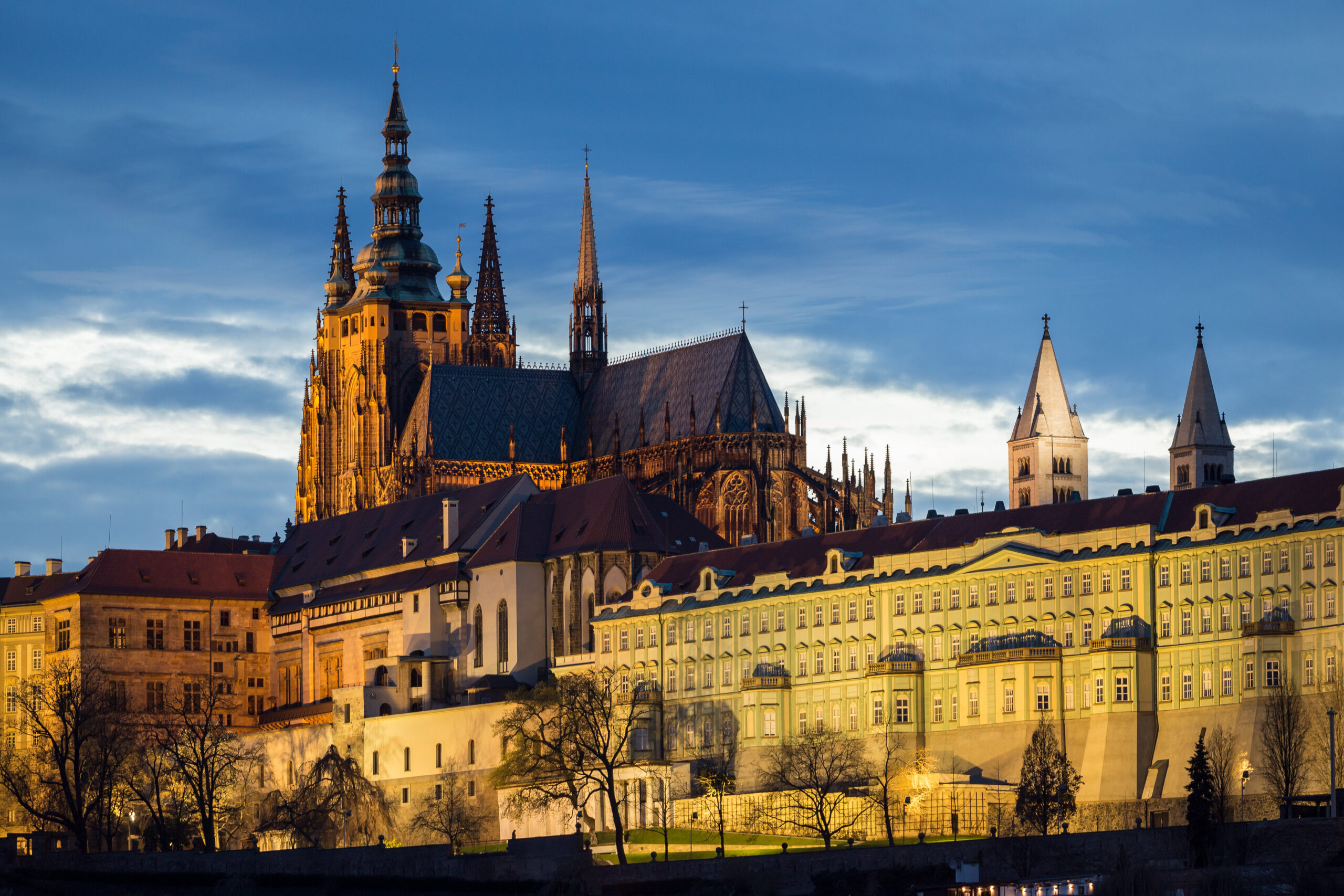 Gothic cathedral with tall spires rising above a row of pastel-green townhouses at dusk.