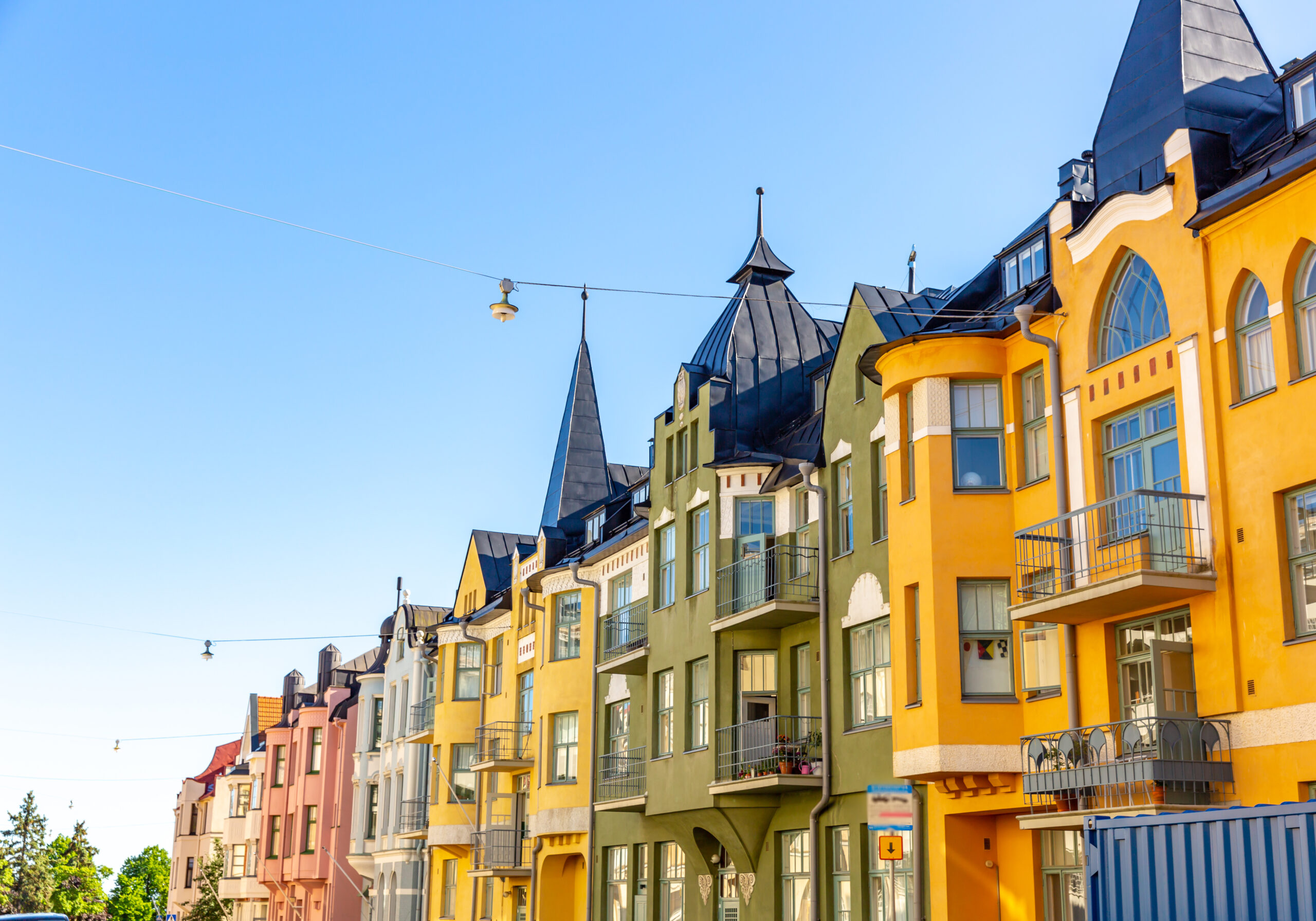 Colorful row of European-style apartment buildings with pointed blue-gray roofs and balconies against a clear blue sky.