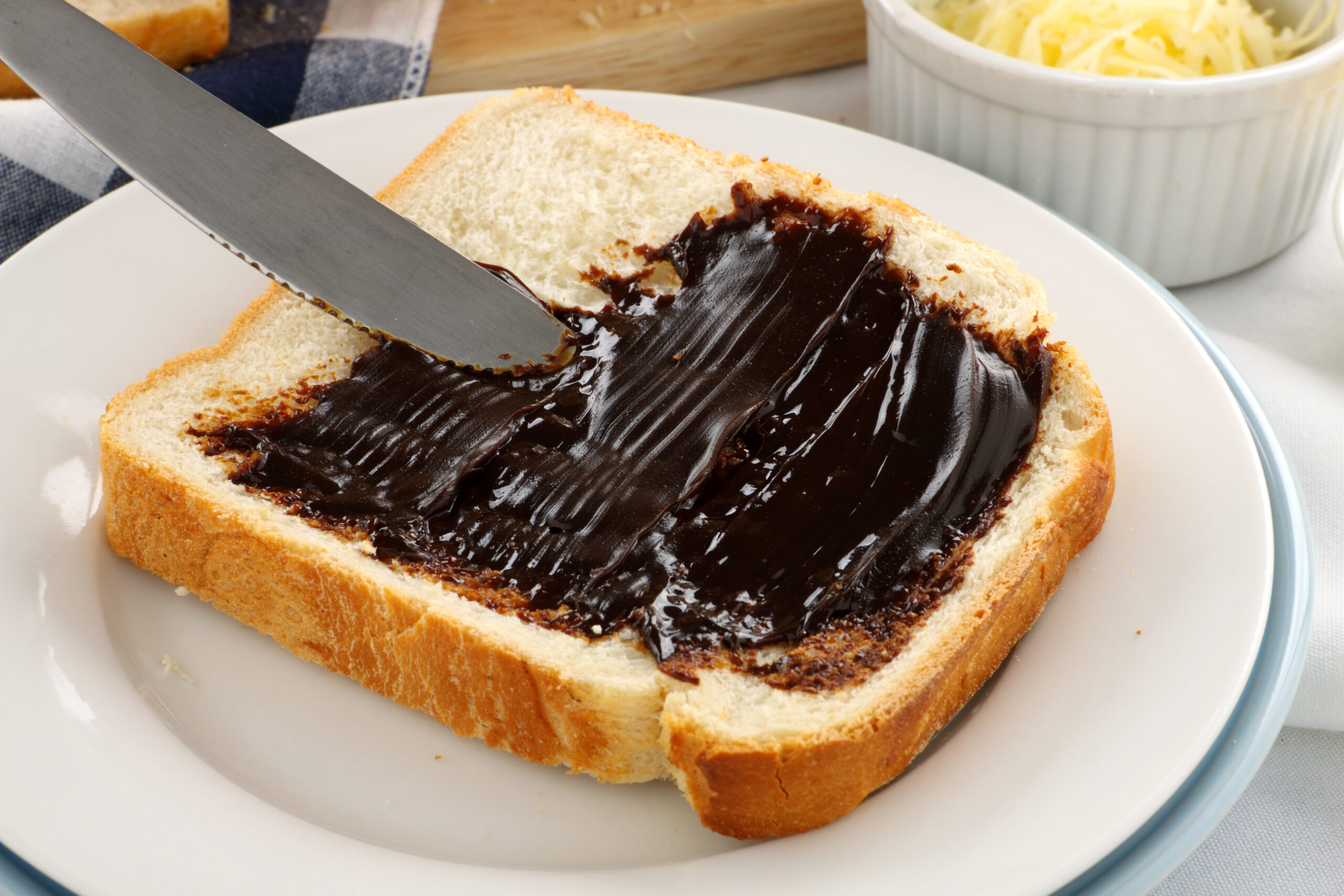 Toast with a thick layer of dark chocolate spread on a white plate, knife resting on the bread edge.