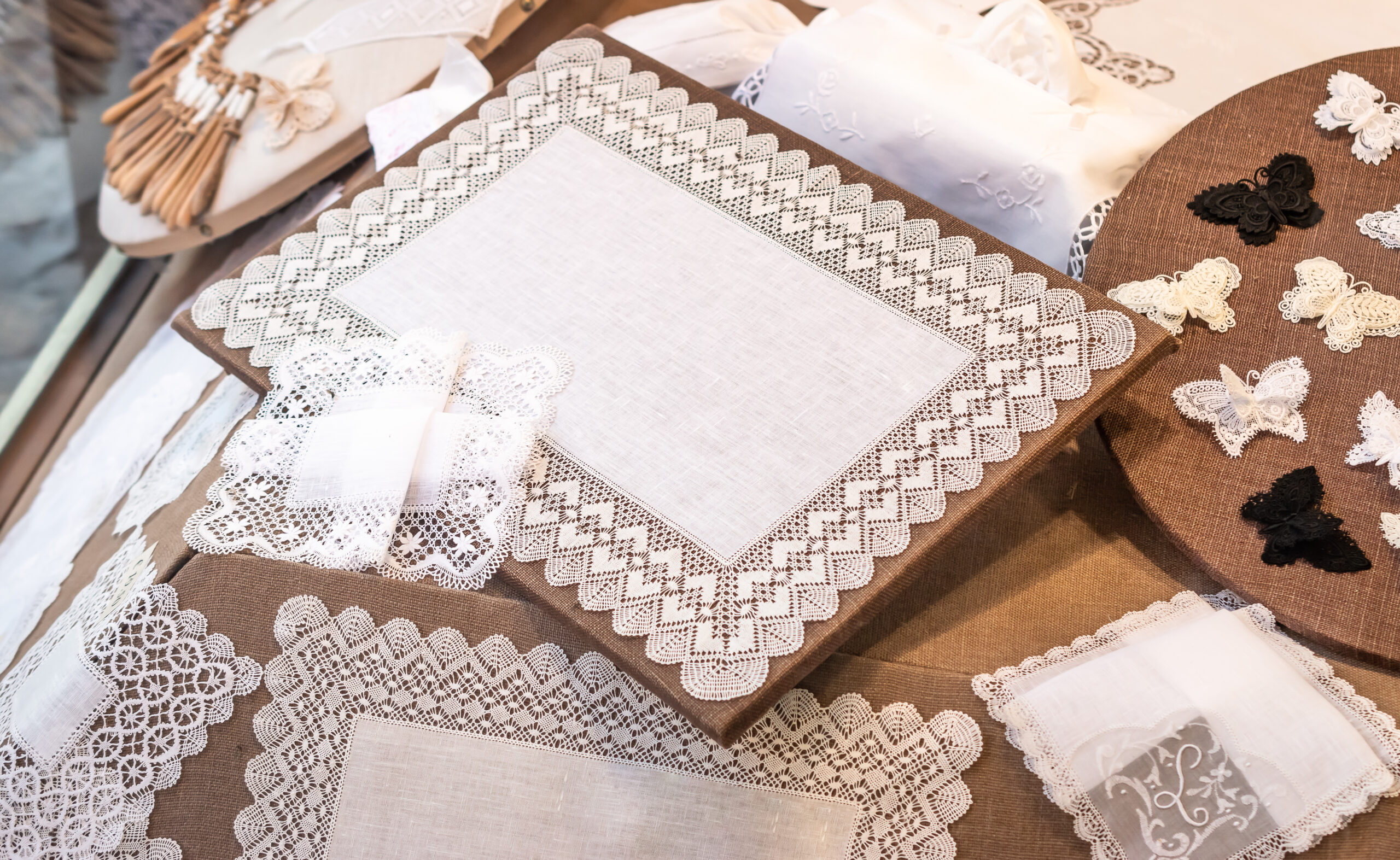 Close-up of white lace doilies and table runners arranged on a brown display surface.