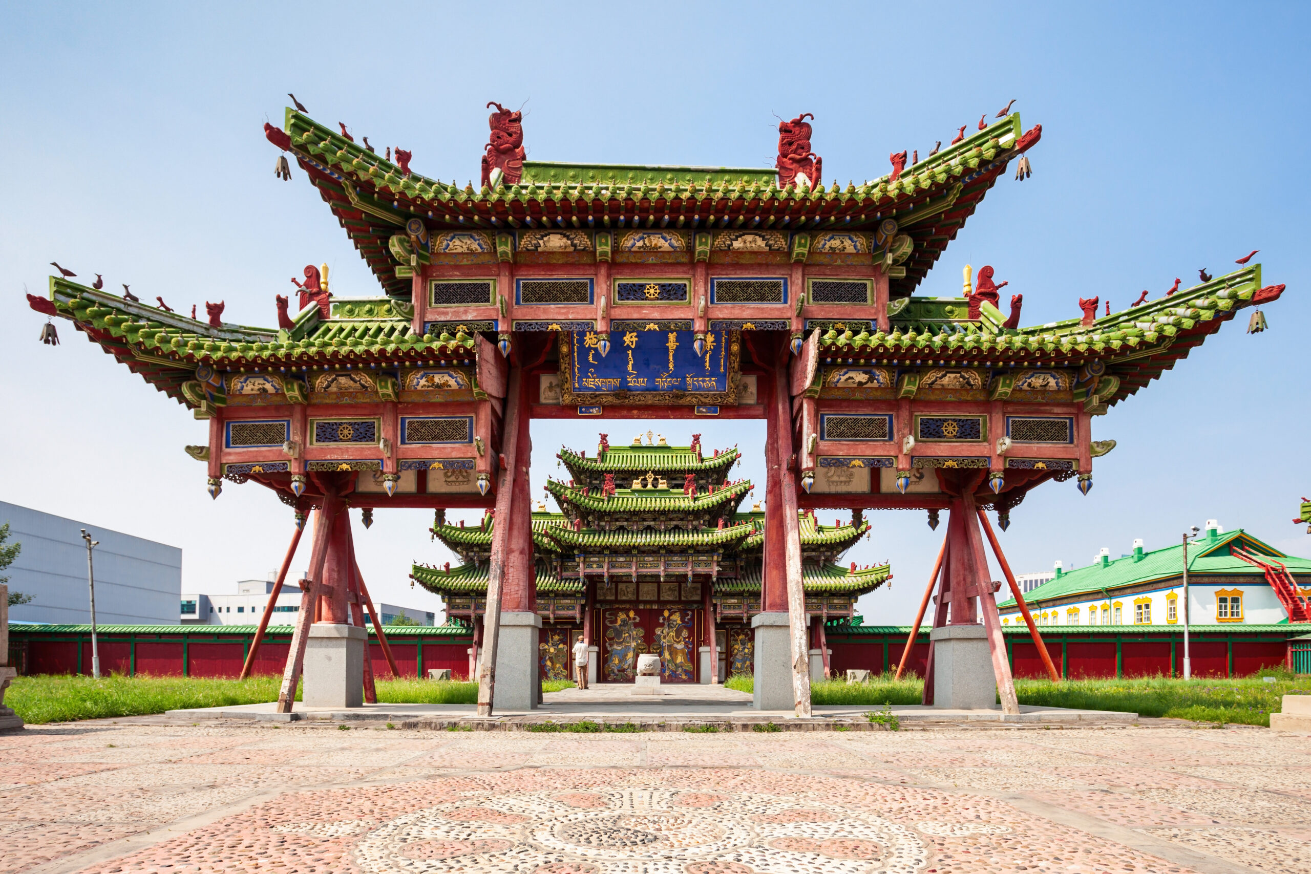 Ornate Chinese temple gateway with red pillars, multicolored eaves and dragon ornaments against a clear blue sky.