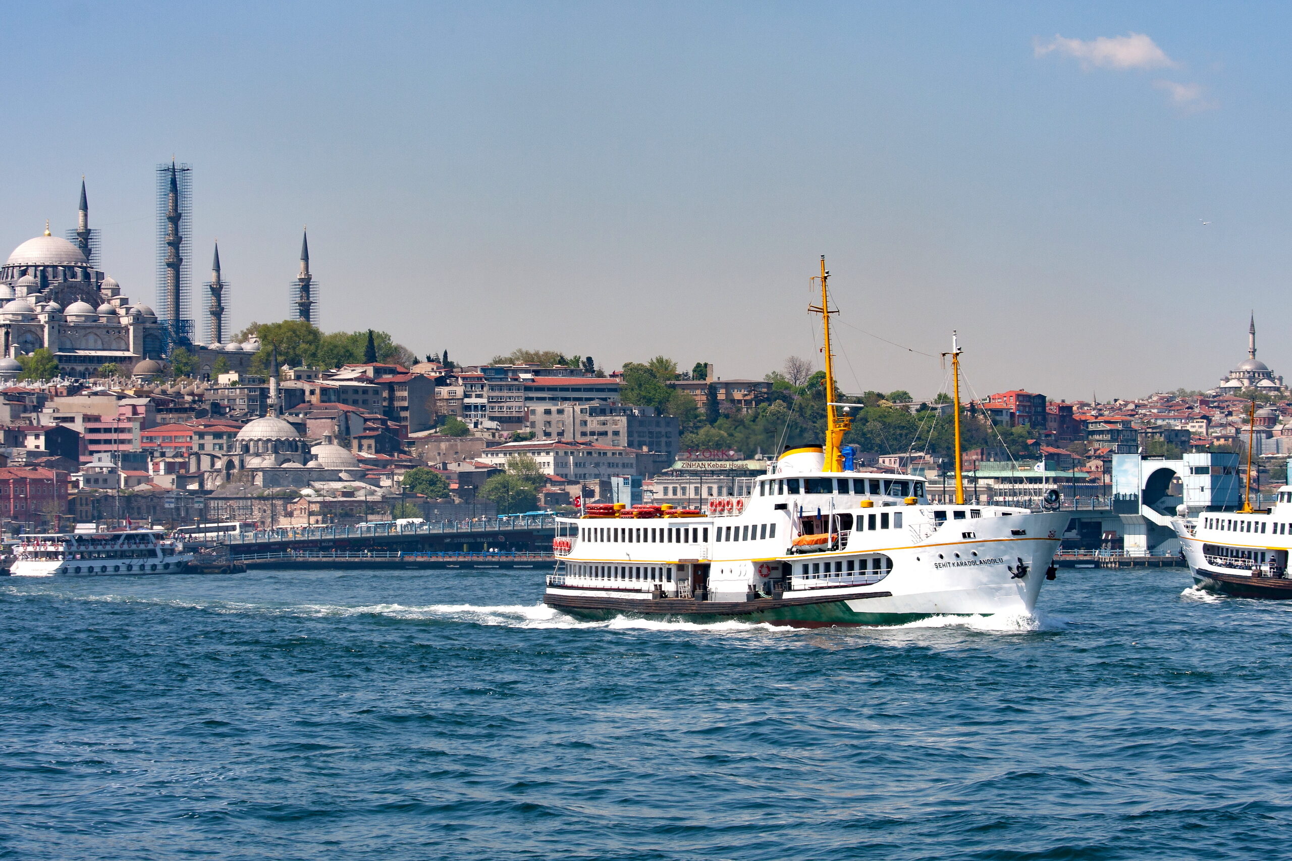 Harbor view of Istanbul with domed mosques and tall minarets along the waterfront and boats on blue water.