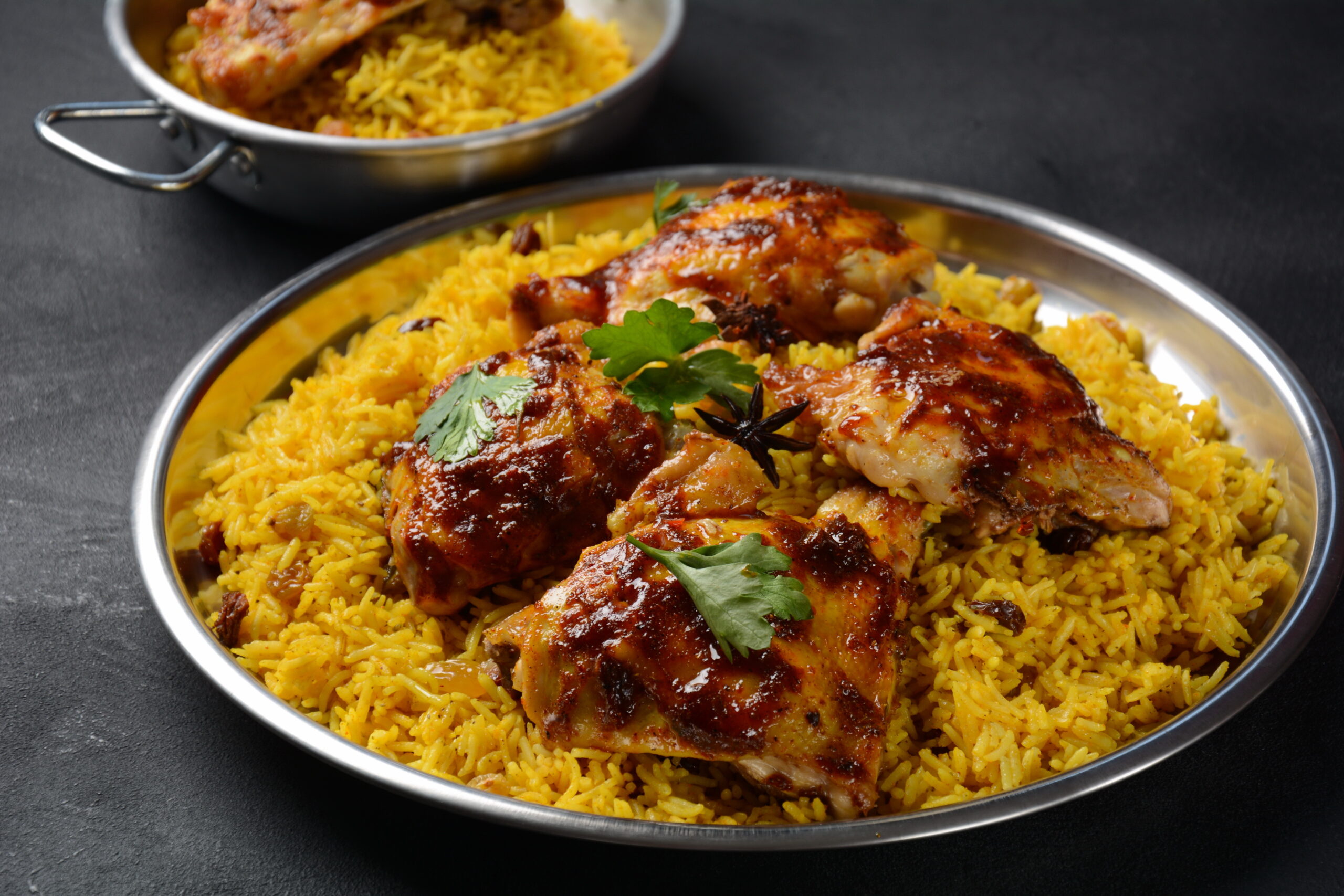 Roasted chicken served over yellow saffron rice with cilantro on a metal plate.