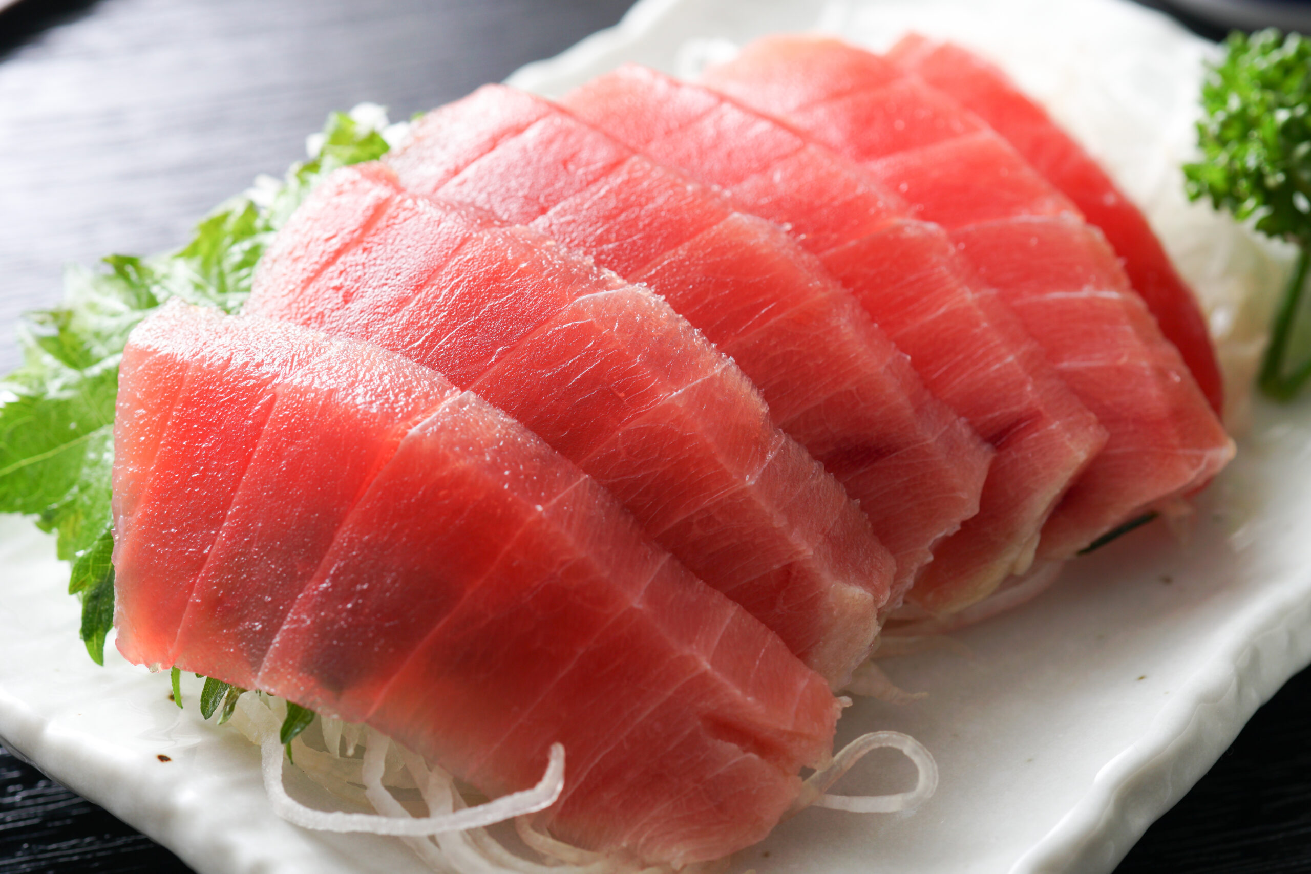 Thinly sliced raw tuna sashimi arranged on a plate with shredded onion and greens garnish