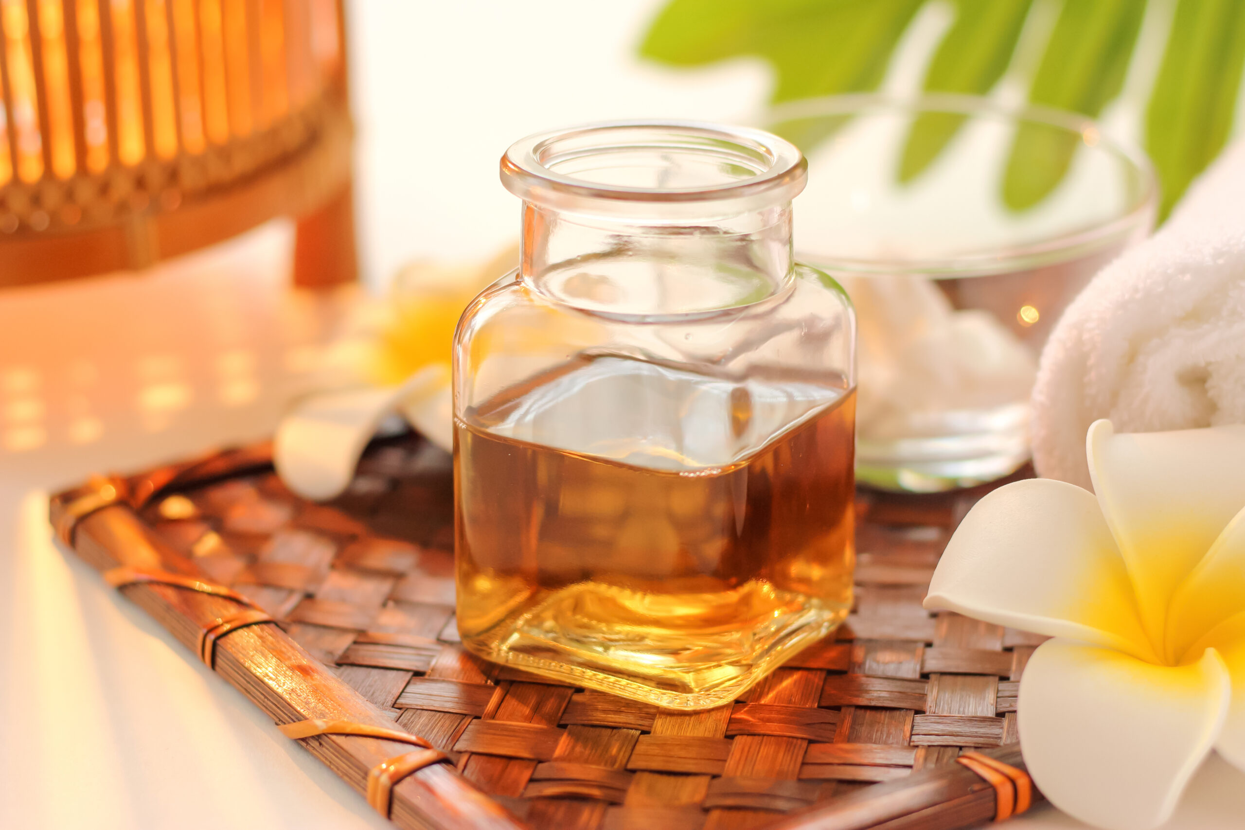 Glass bottle of amber oil on a woven mat with spa items in soft focus around it