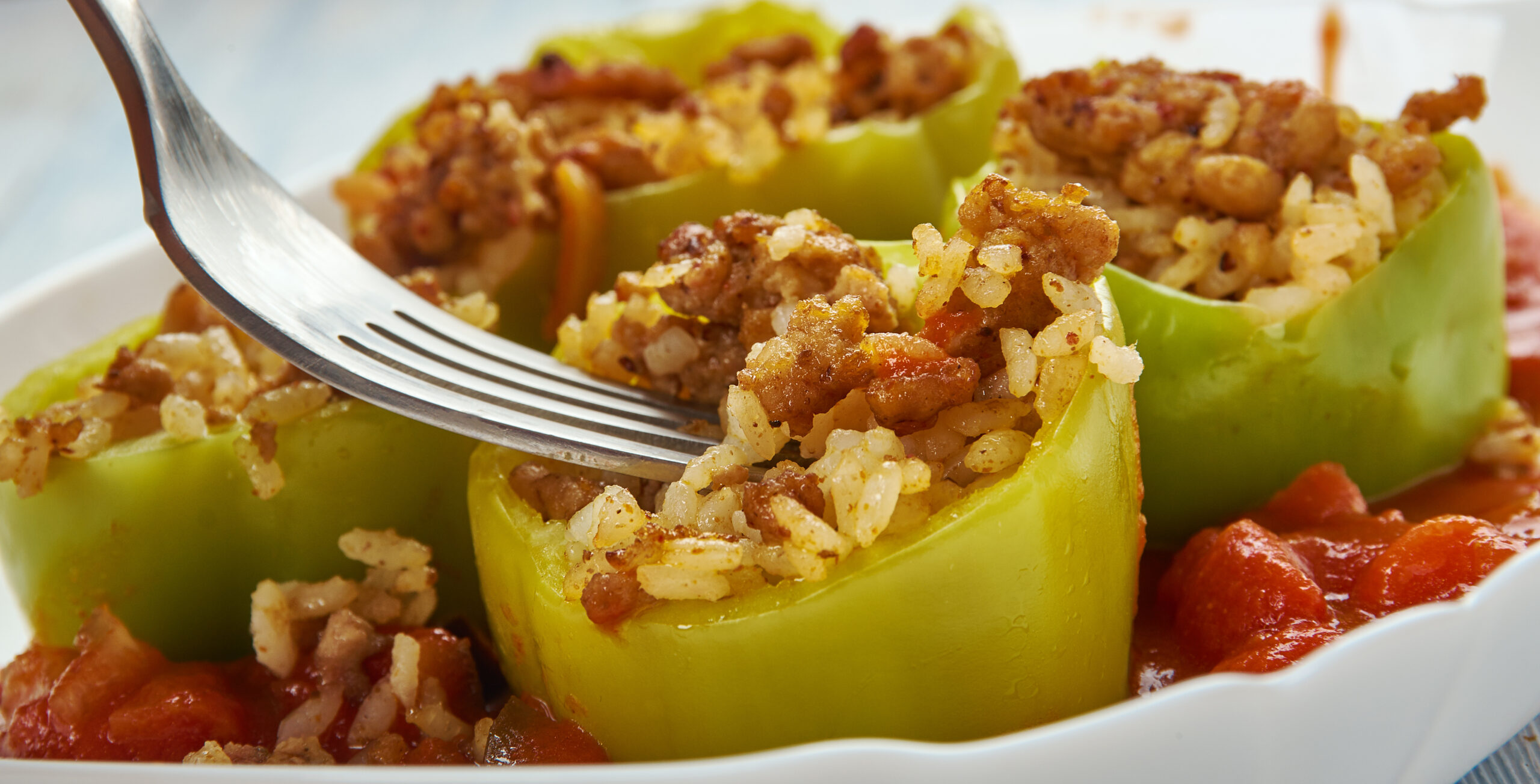 Green bell peppers stuffed with seasoned rice and ground meat, fork hovering over filling