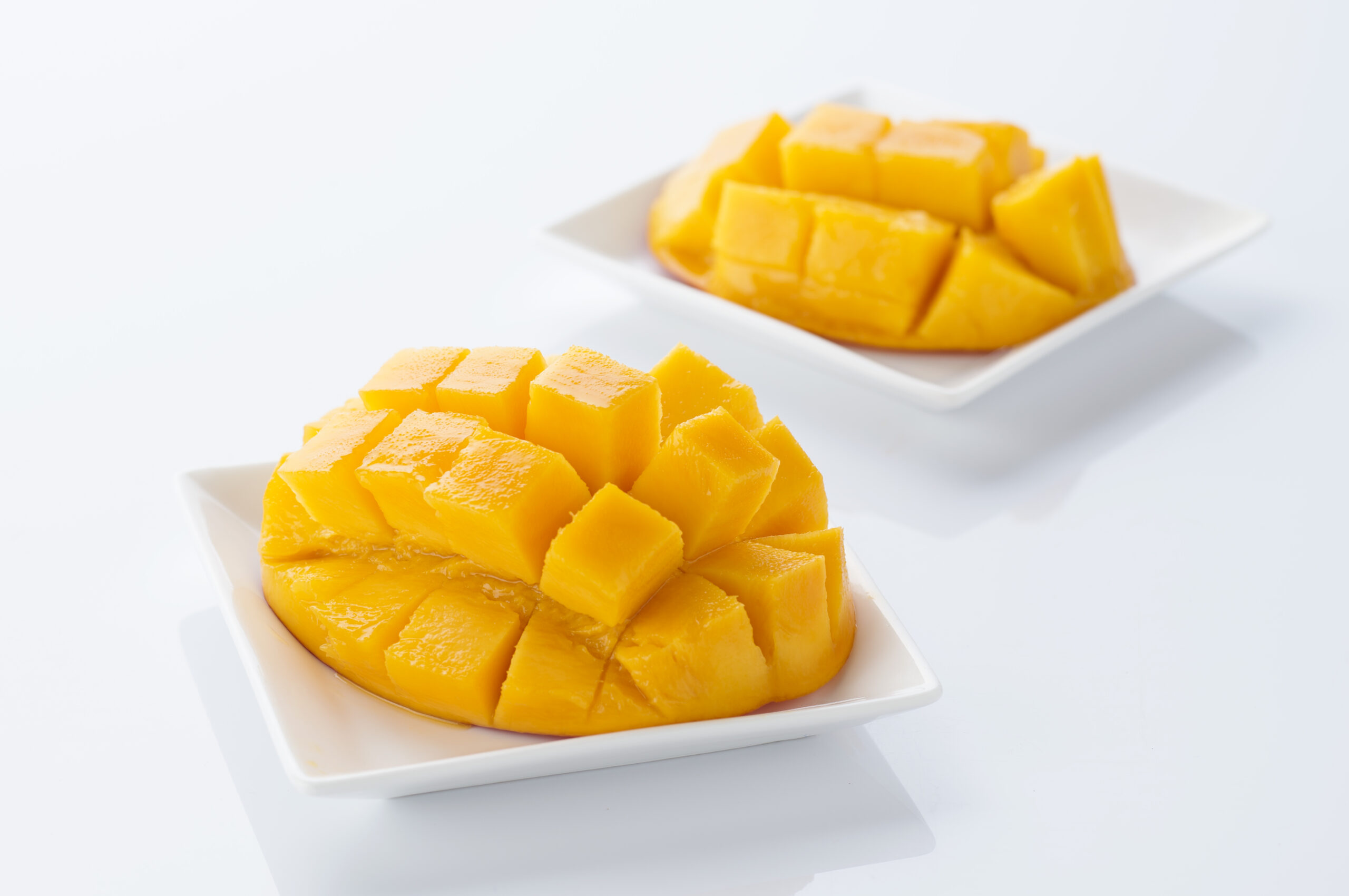 Diced mango chunks arranged on a white square plate with a blurred background, bright yellow-orange fruit.