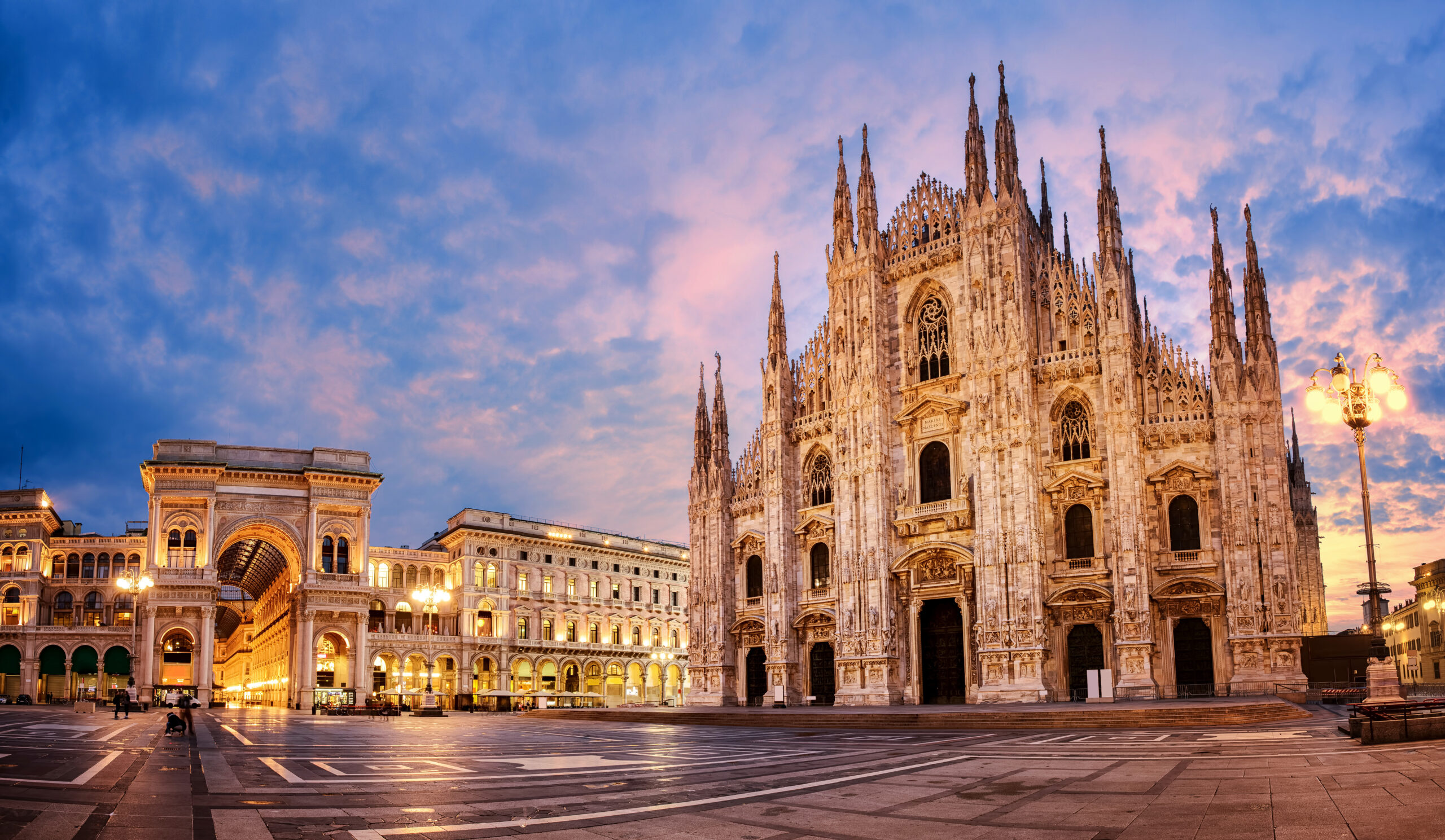 Milan Cathedral (Duomo di Milano) with ornate Gothic facade at sunset in Piazza del Duomo, arcades and warm streetlights nearby