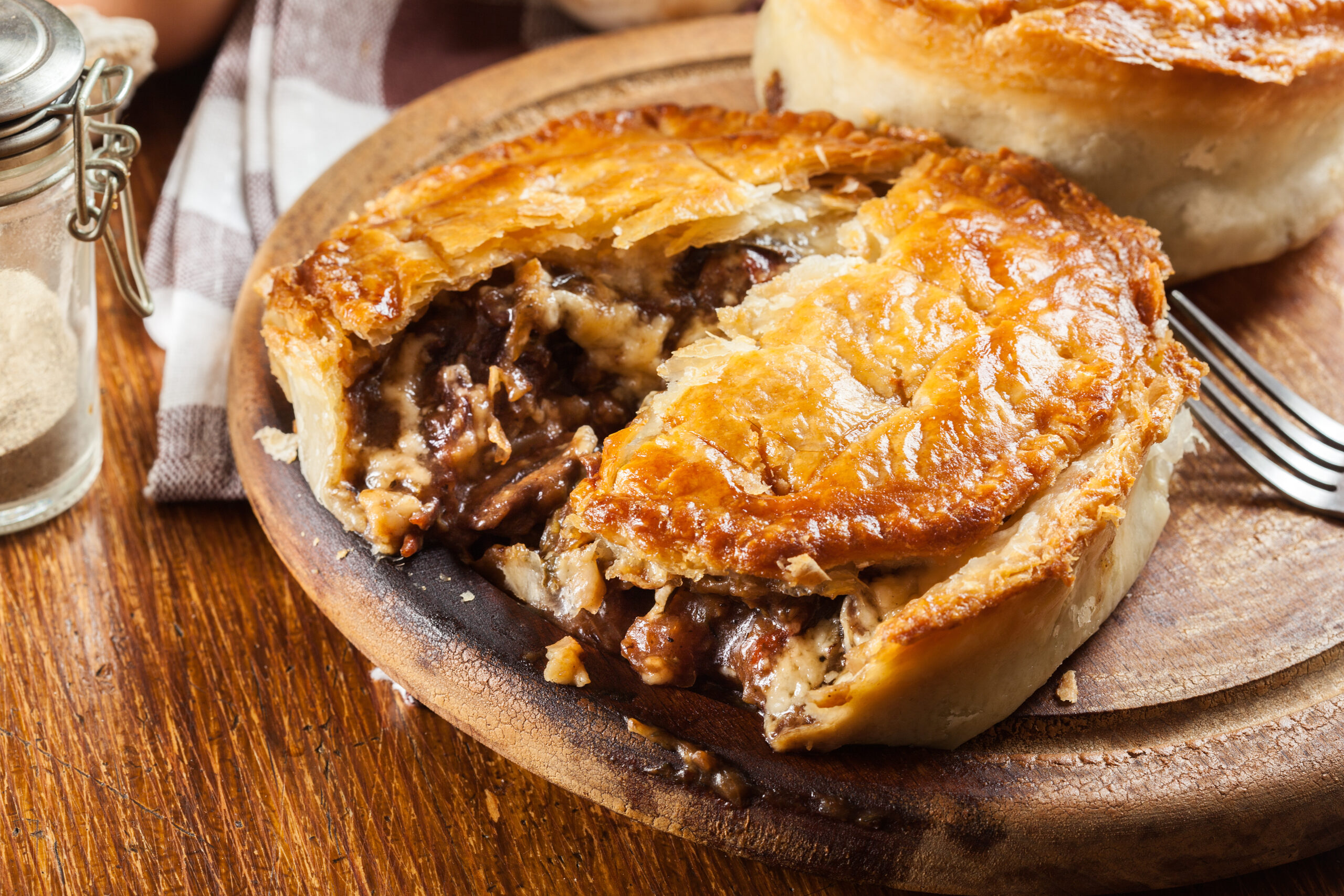 Slice of beef pot pie on a wooden board, flaky golden crust and beef filling visible where cut open