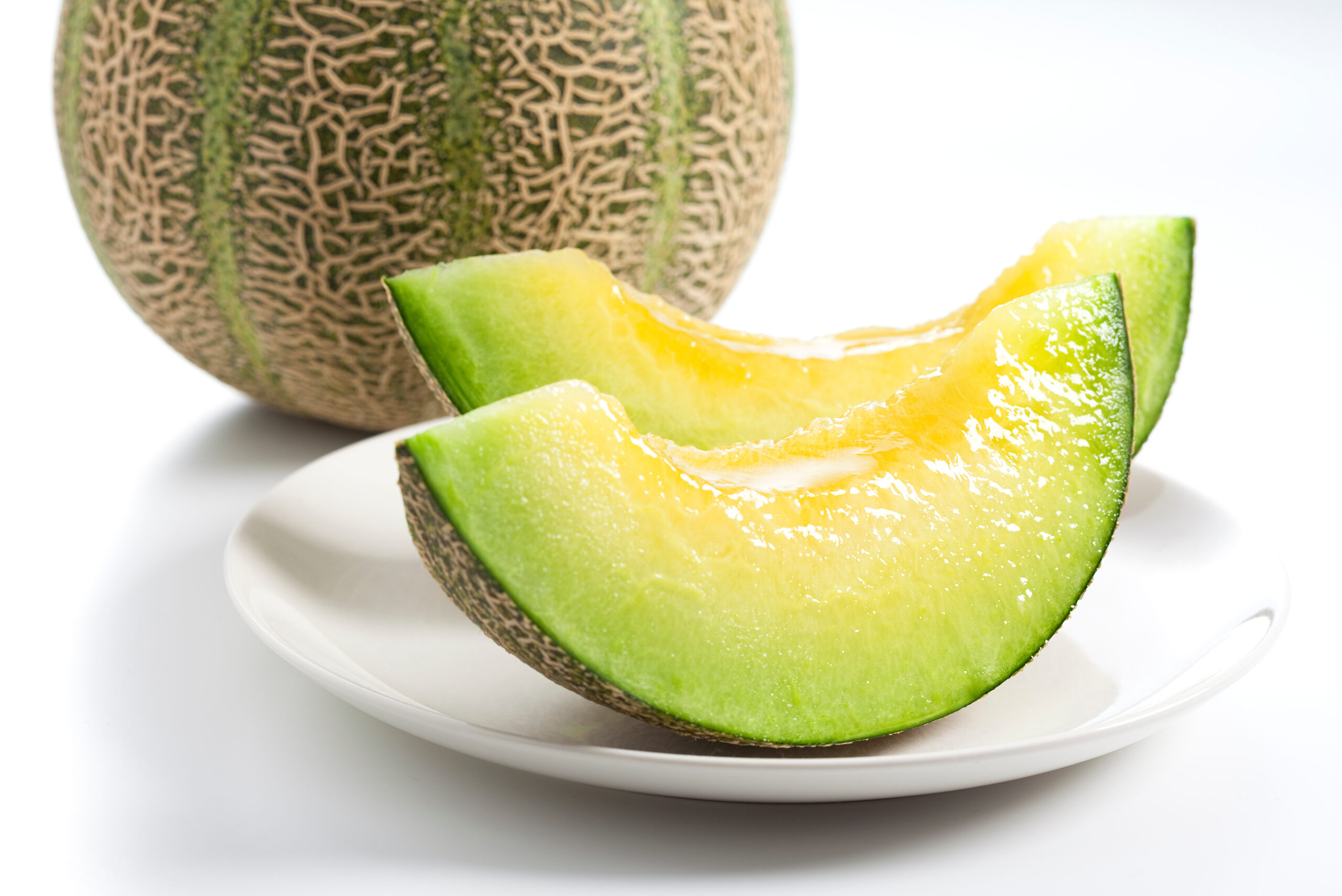 Slices of cantaloupe arranged on a white plate with a whole cantaloupe in the background.