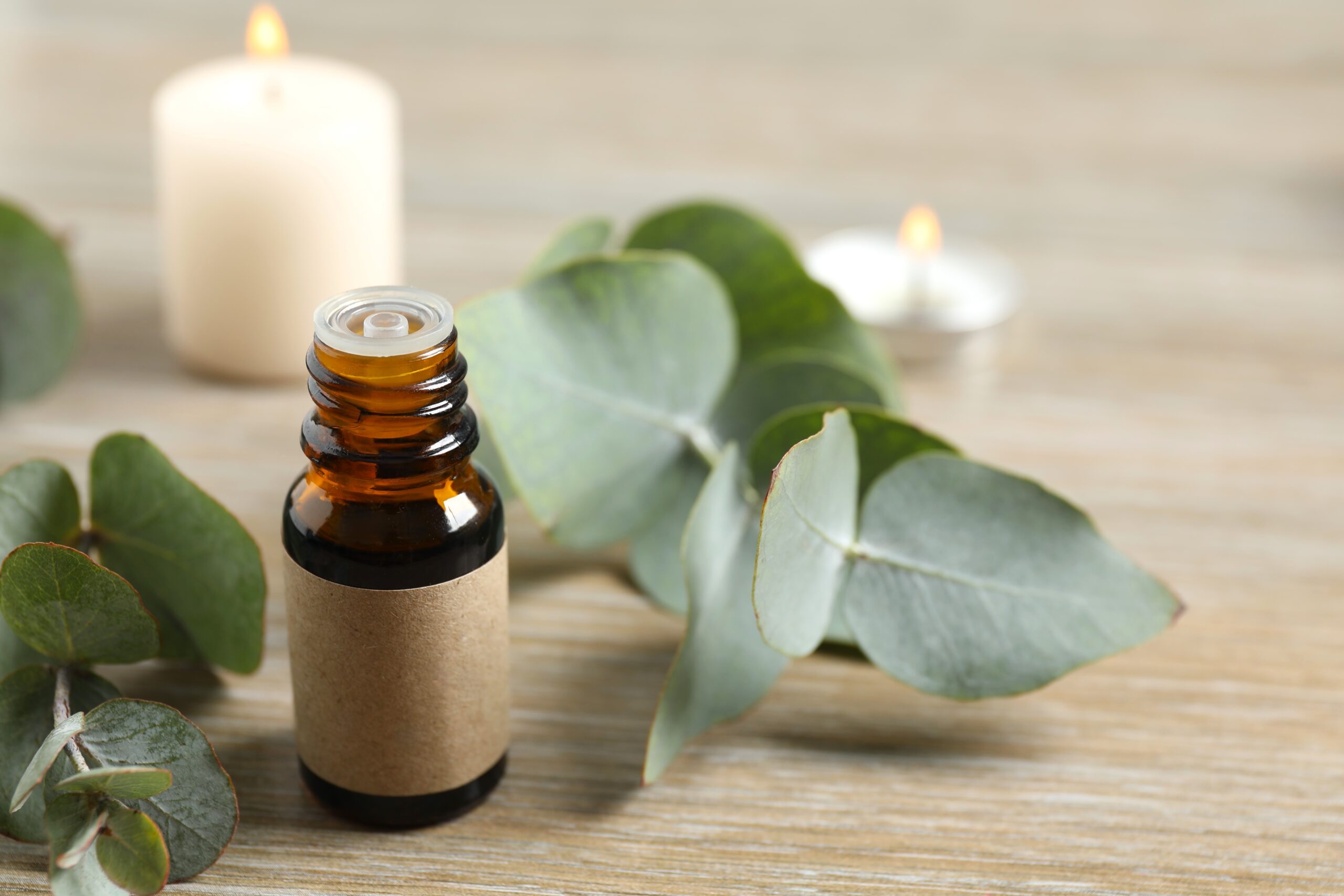 Brown glass essential oil bottle with dropper, surrounded by eucalyptus leaves on a wooden surface.