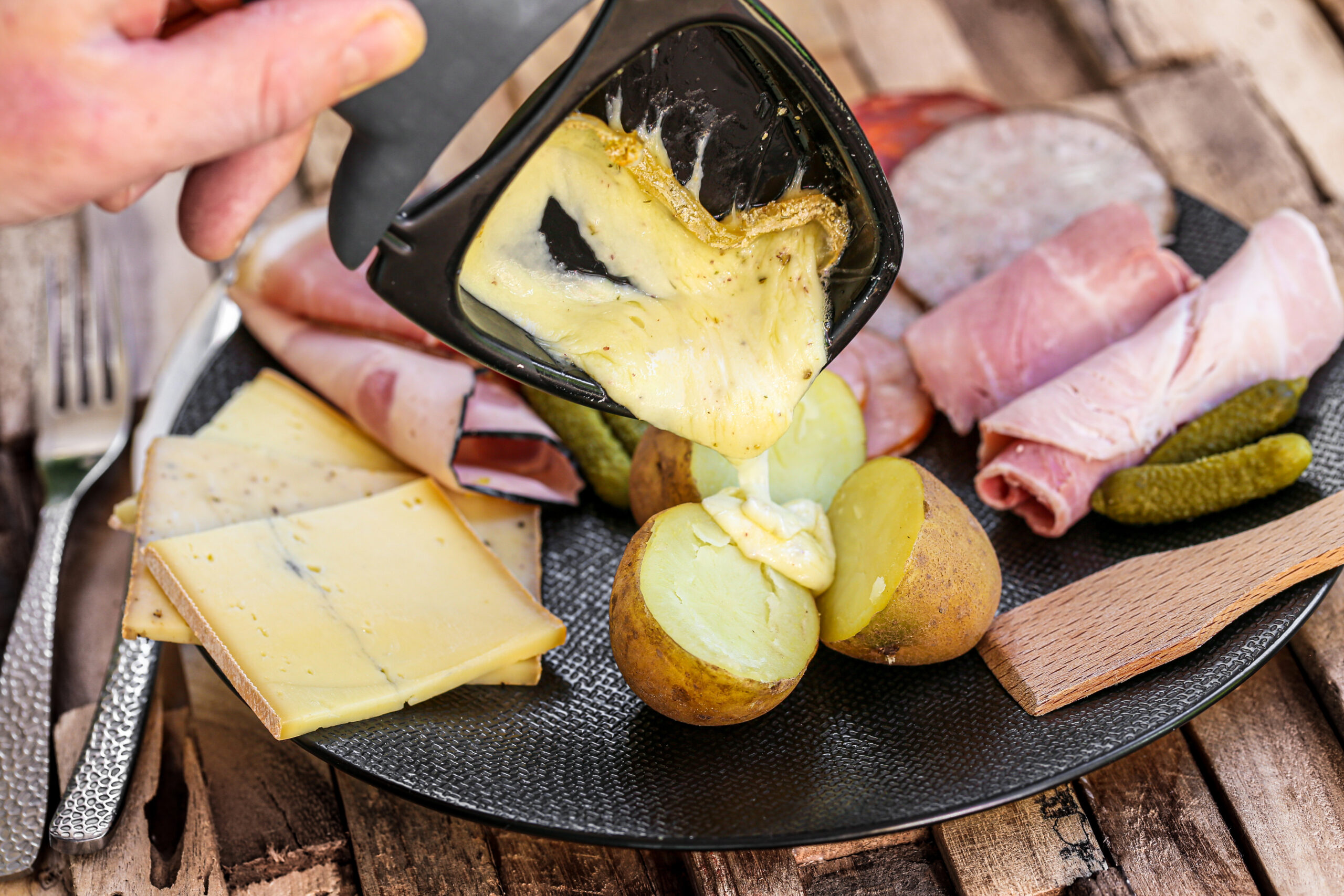 Close-up of melted cheese being poured onto a charcuterie board with potatoes and sliced meats.