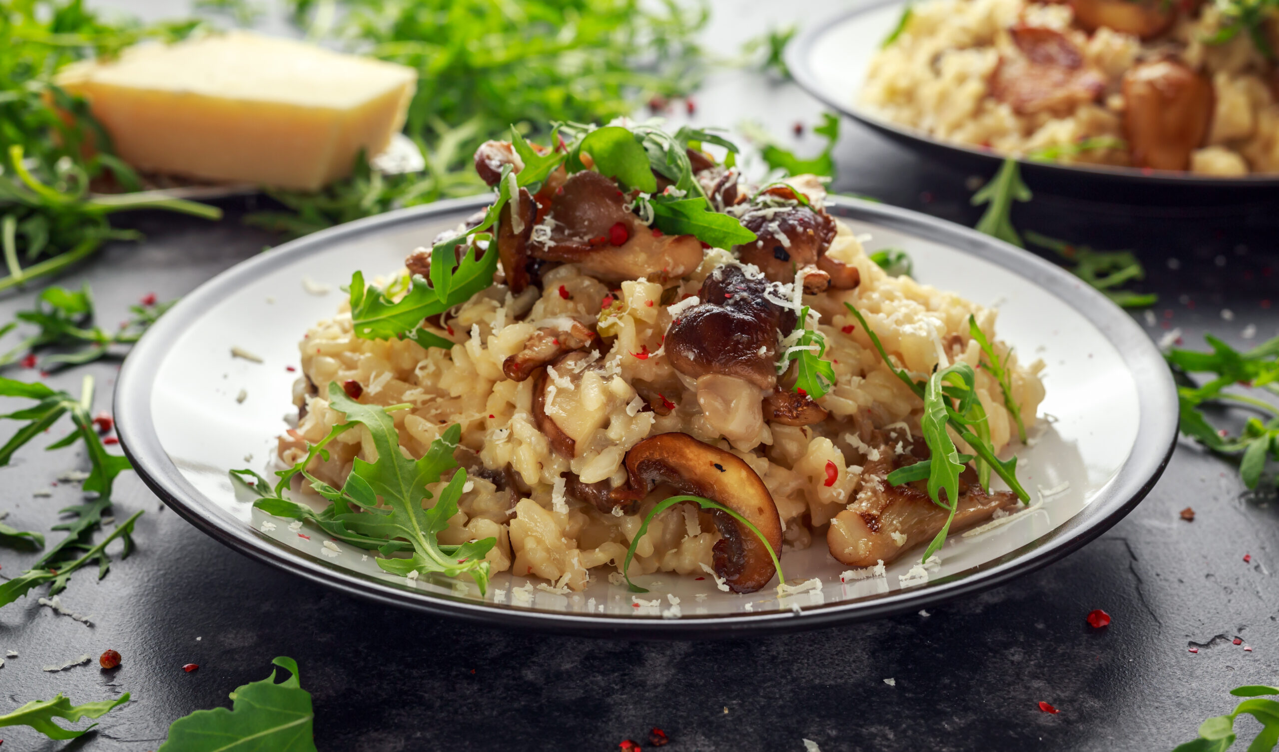 Creamy mushroom risotto topped with arugula and shaved Parmesan on a white plate.