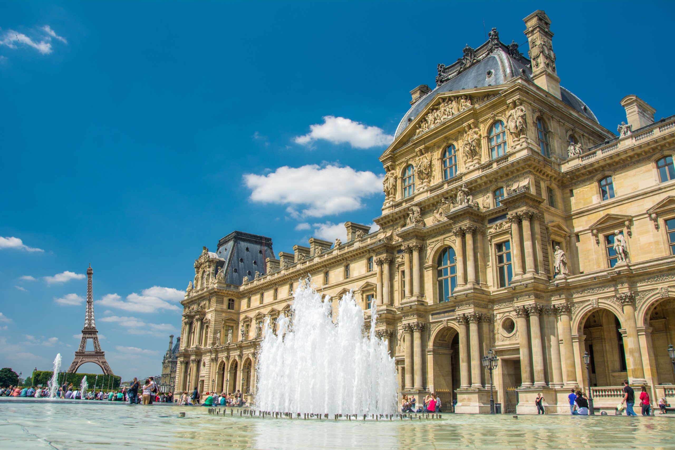 Ornate Parisian facade with statues and arched windows, a large fountain in the foreground, and the Eiffel Tower in the distance.