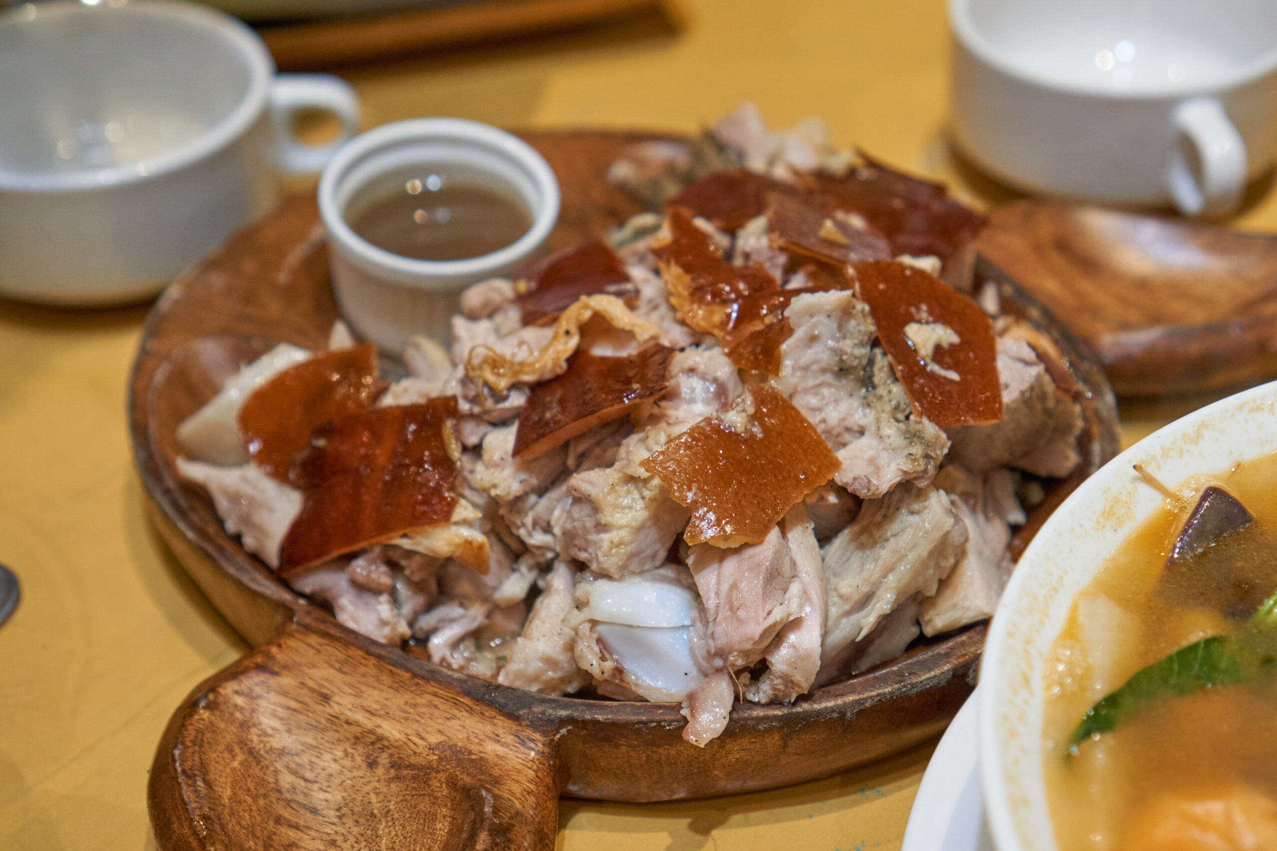 Pulled pork with crispy crackling on a wooden platter, with small cups in the background.