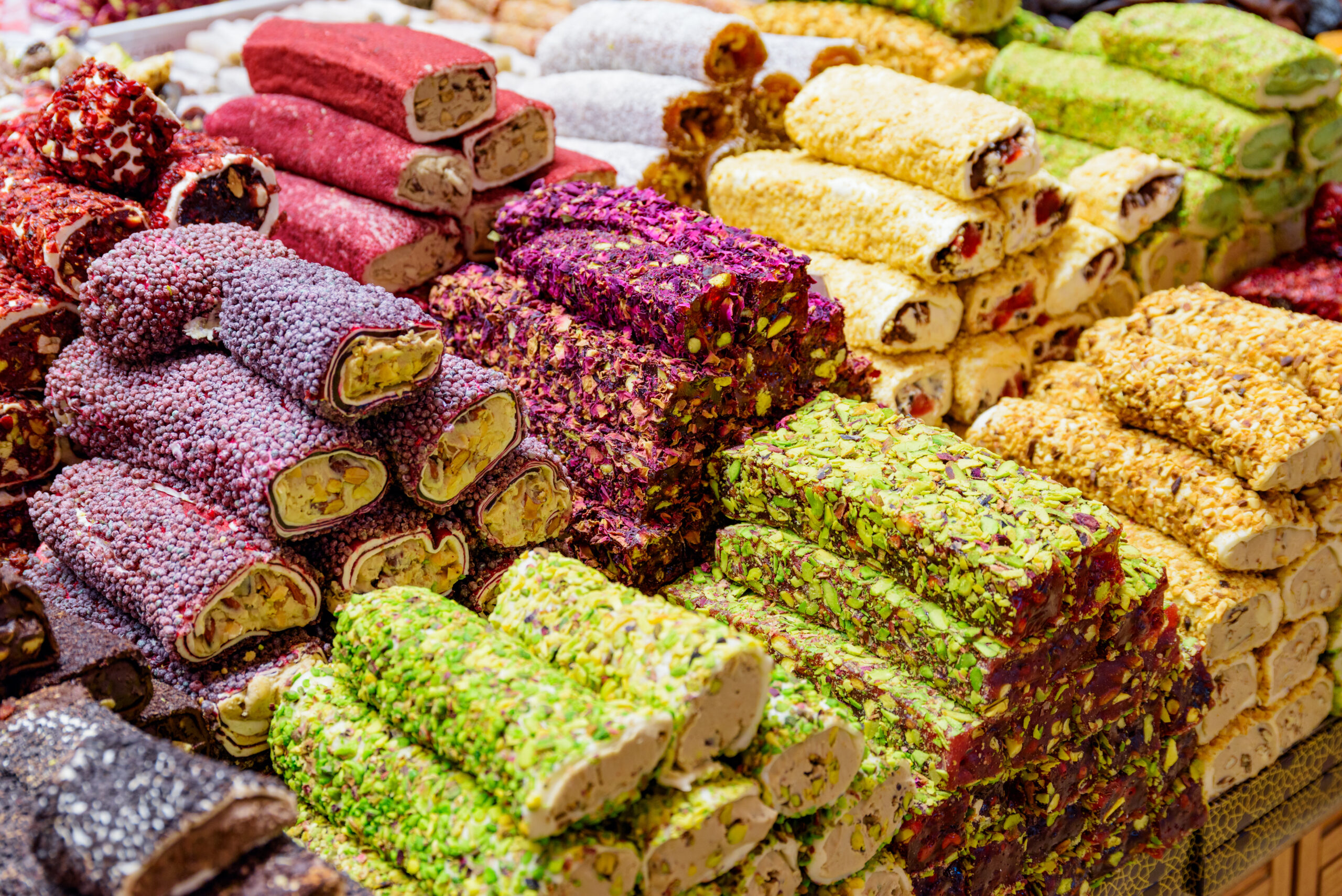 Stacked colorful Turkish delight sweets coated with nuts and coconut, piled in a display.