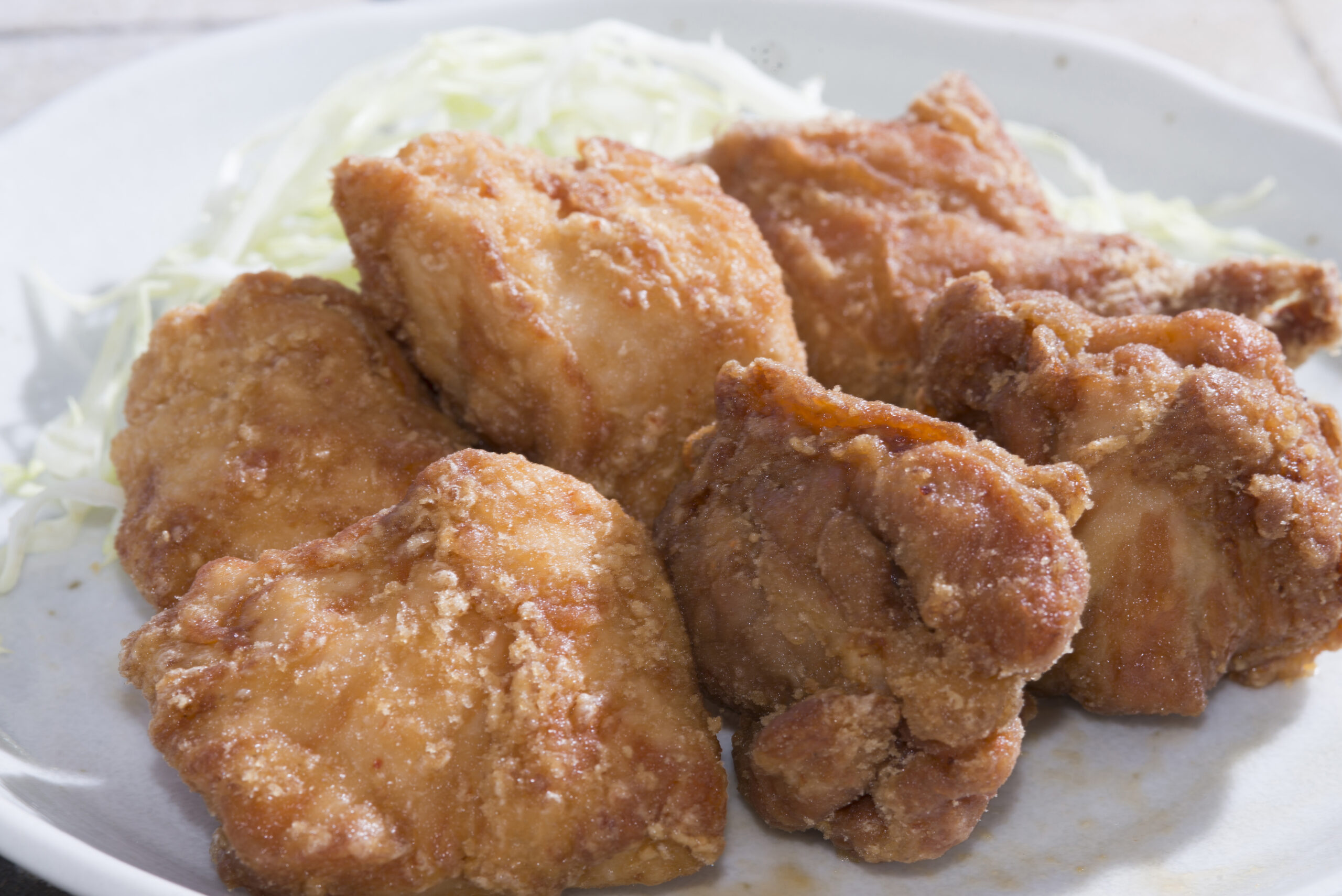 Crispy fried chicken pieces on a plate with shredded cabbage in the background.