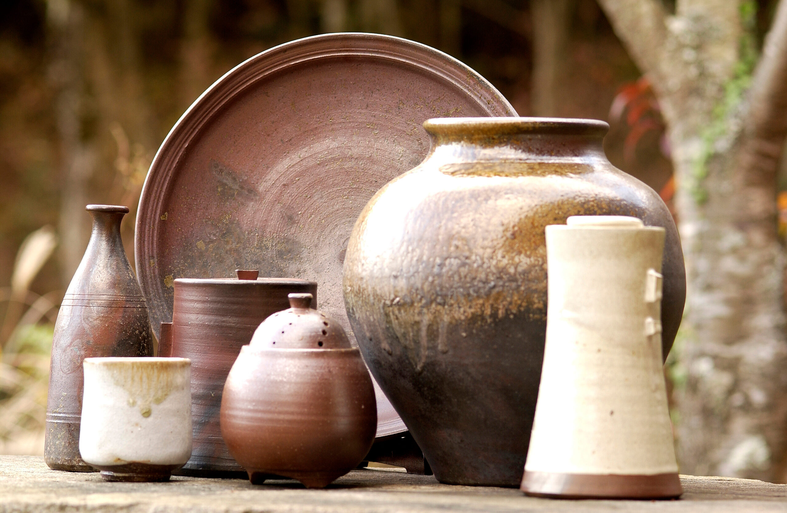 Assorted ceramic pots and vases arranged on a wooden surface outdoors.