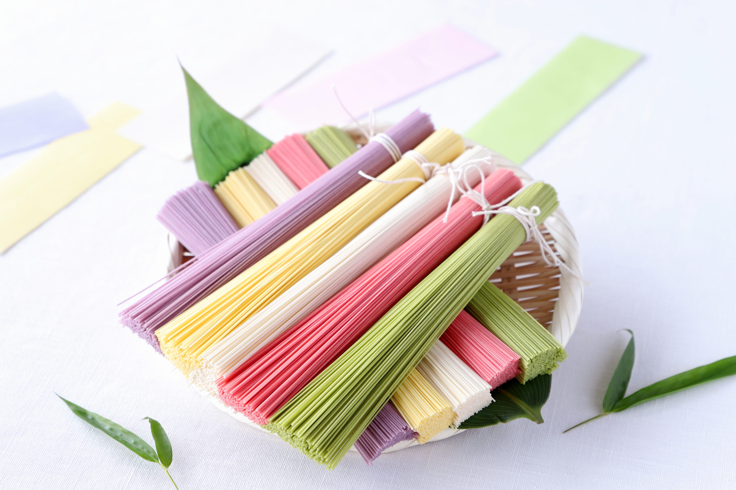 Basket of pastel-colored paper straws arranged in rows on a white surface with greenery accents in the background