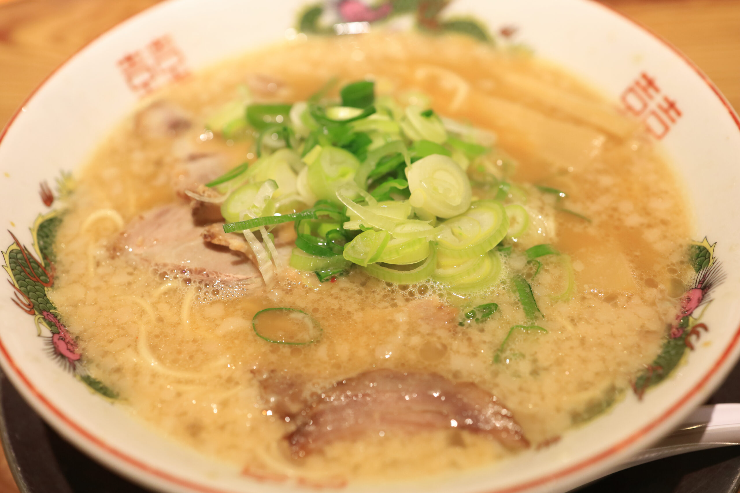 Bowl of miso ramen topped with sliced green onions and pork, in a decorative ceramic dish.
