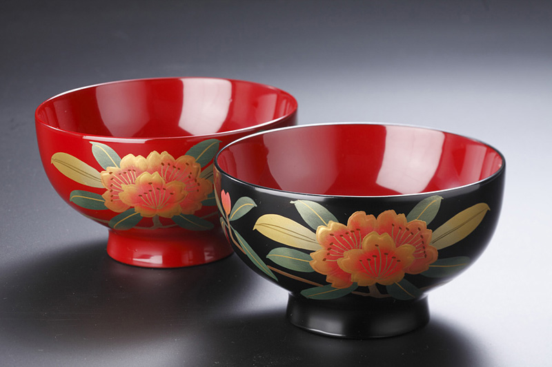 Two lacquer bowls with orange floral patterns on red and black backgrounds, set on a dark surface.