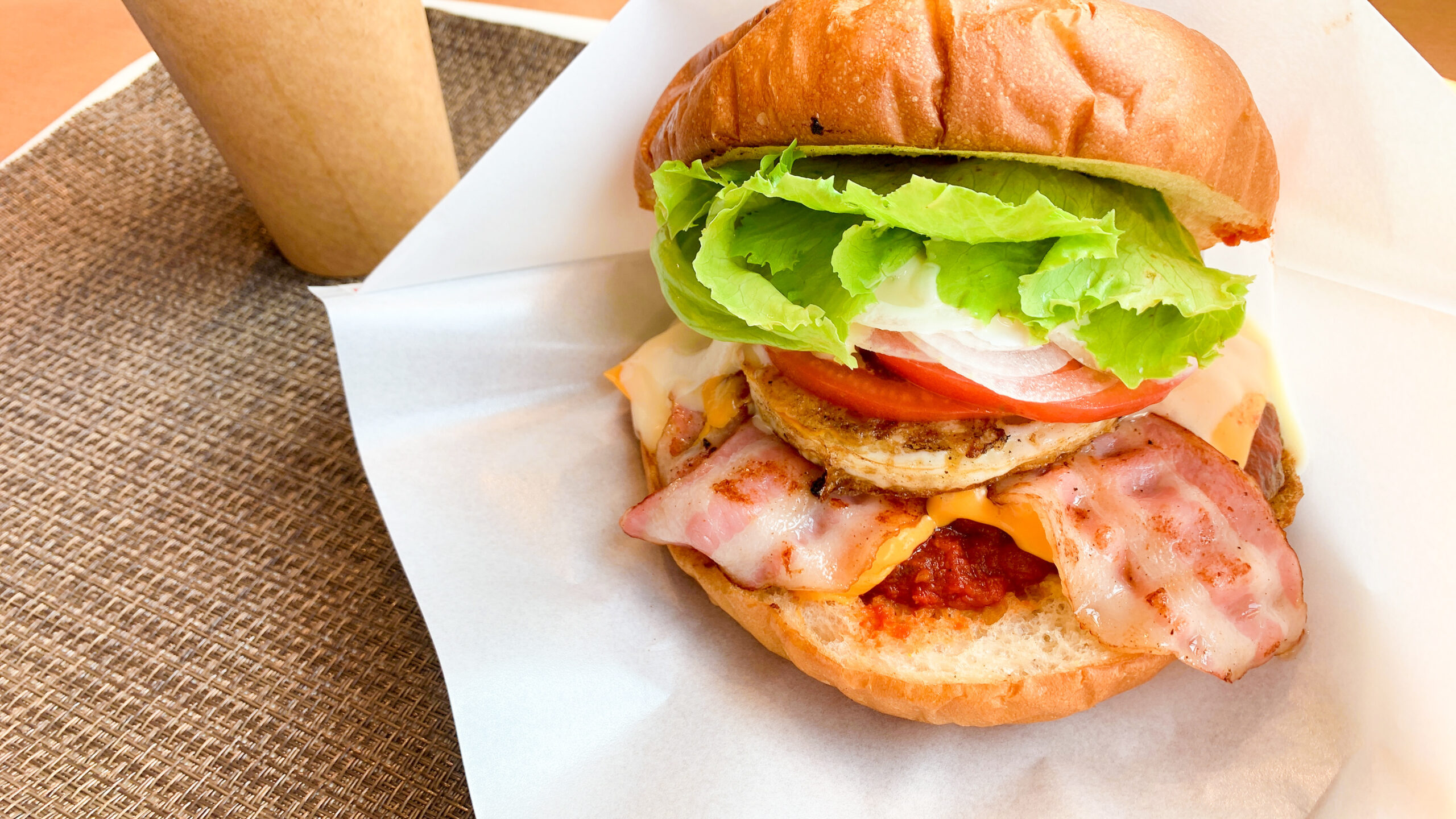 Close-up of a bacon cheeseburger with lettuce, tomato, onion, melted cheese, on a toasted bun with parchment paper.