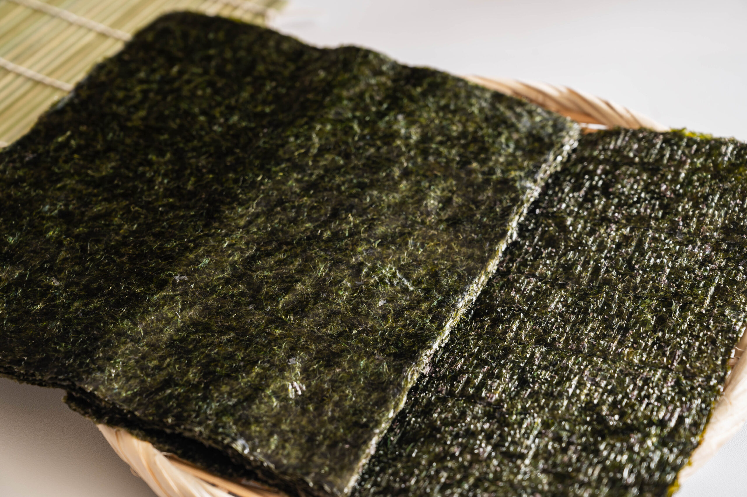 Bundles of dark green nori seaweed sheets in a wicker basket, ready for sushi.