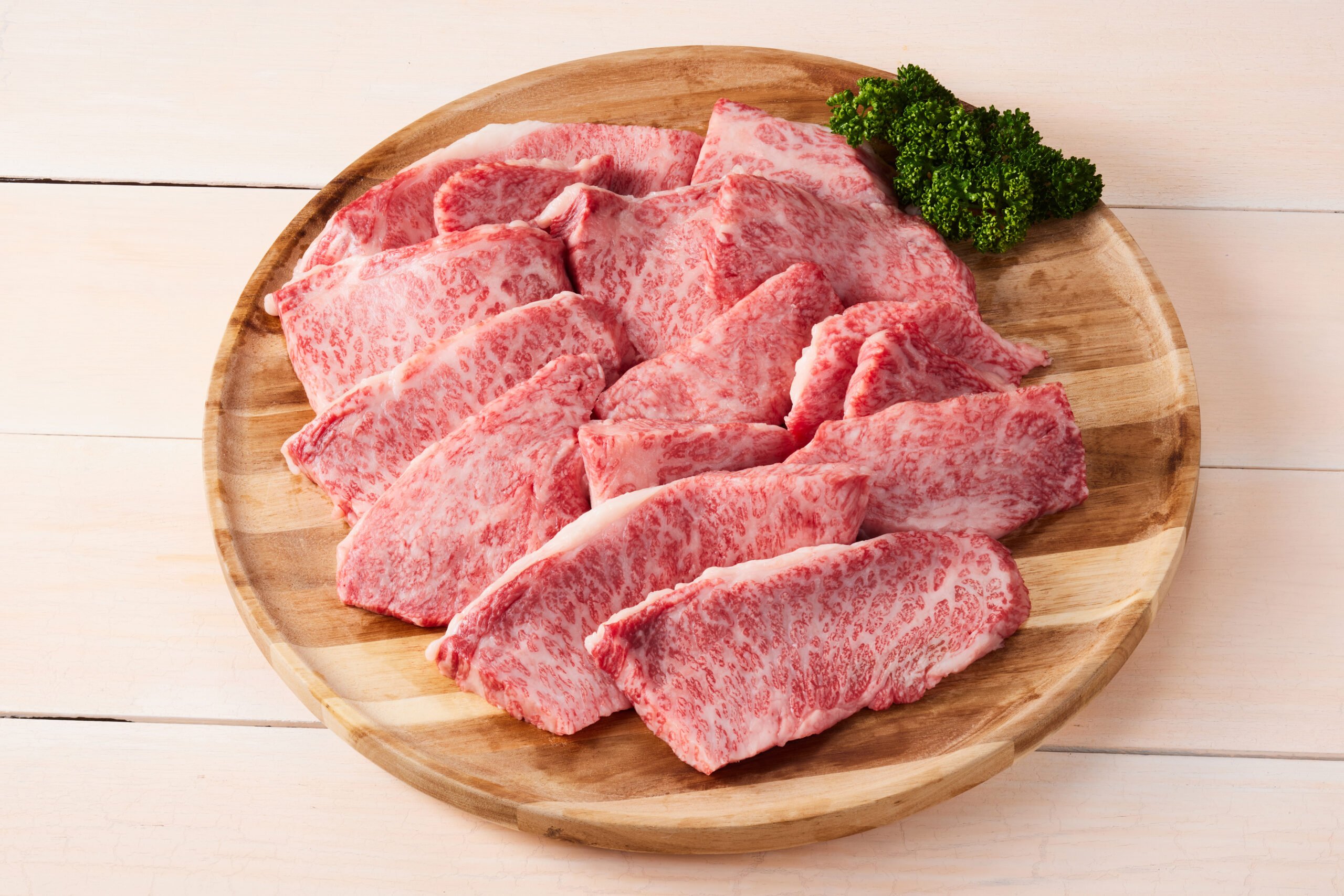 Sliced marbled beef arranged on a round wooden cutting board with parsley garnish