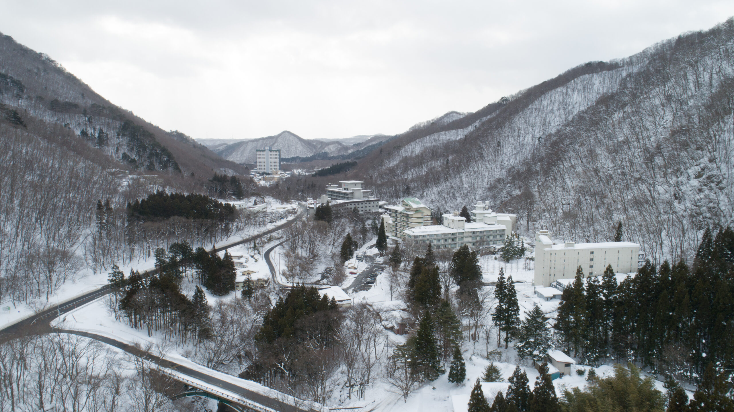 Snow-covered mountain valley with a small town, winding roads, and leafless trees in winter scenery.