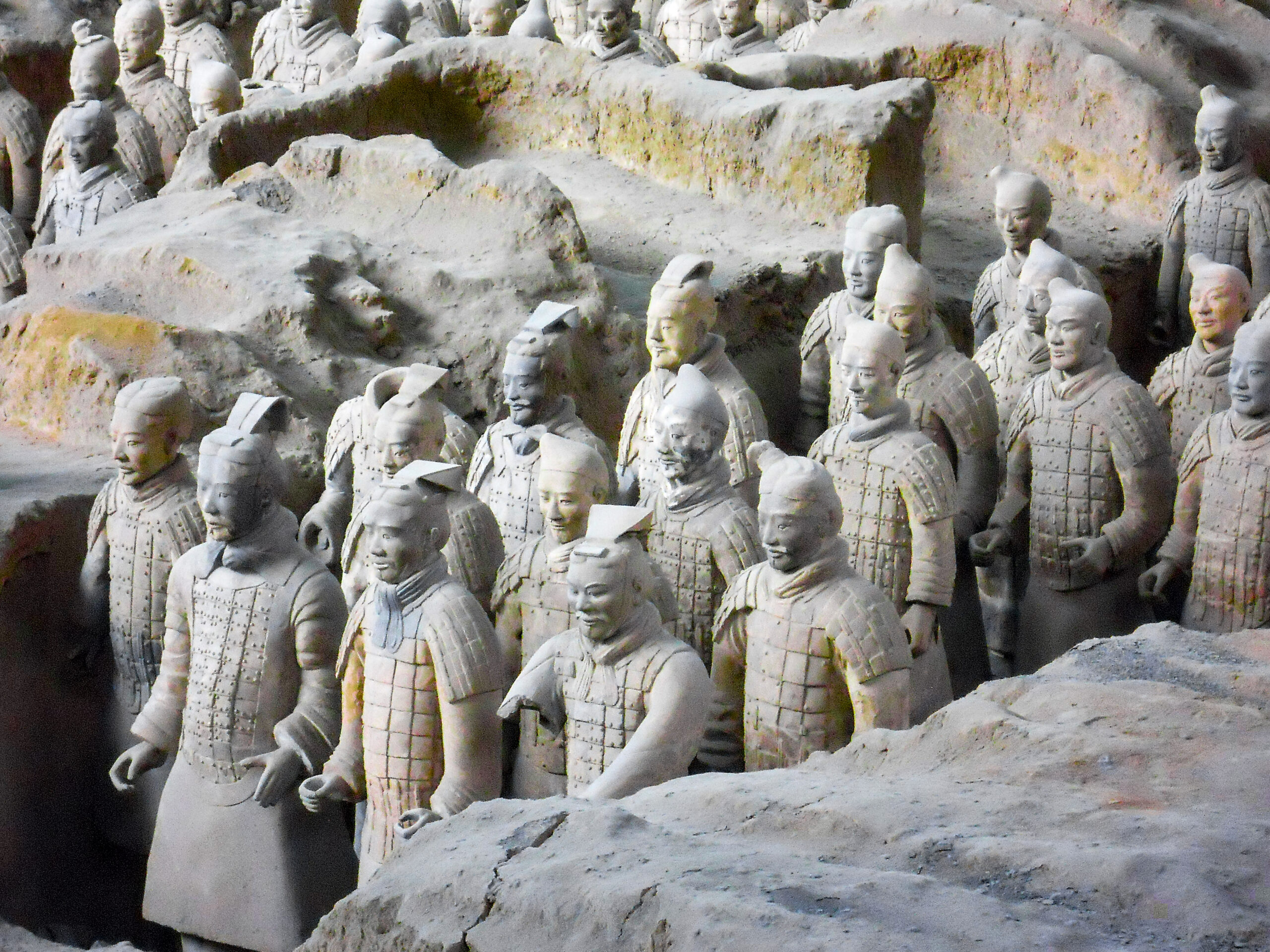 Rows of life-sized Terracotta Army soldiers standing in a dusty excavation pit.