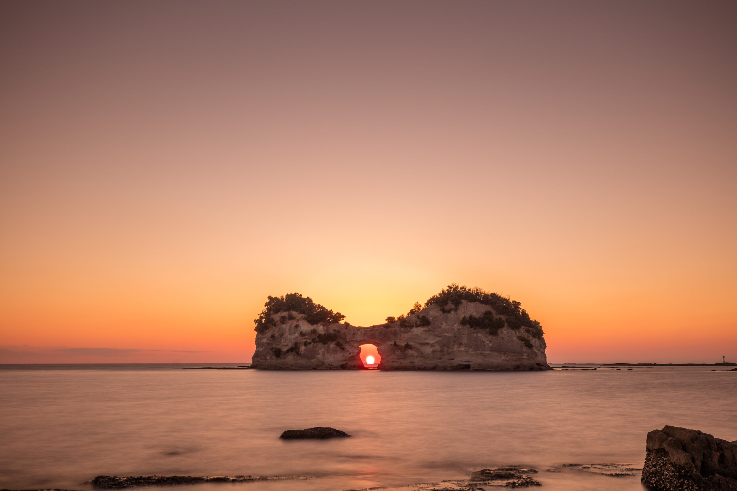 Sunset over the sea with a rocky arch island; the sun visible through the arch stand-in for the sunset light entering the opening.