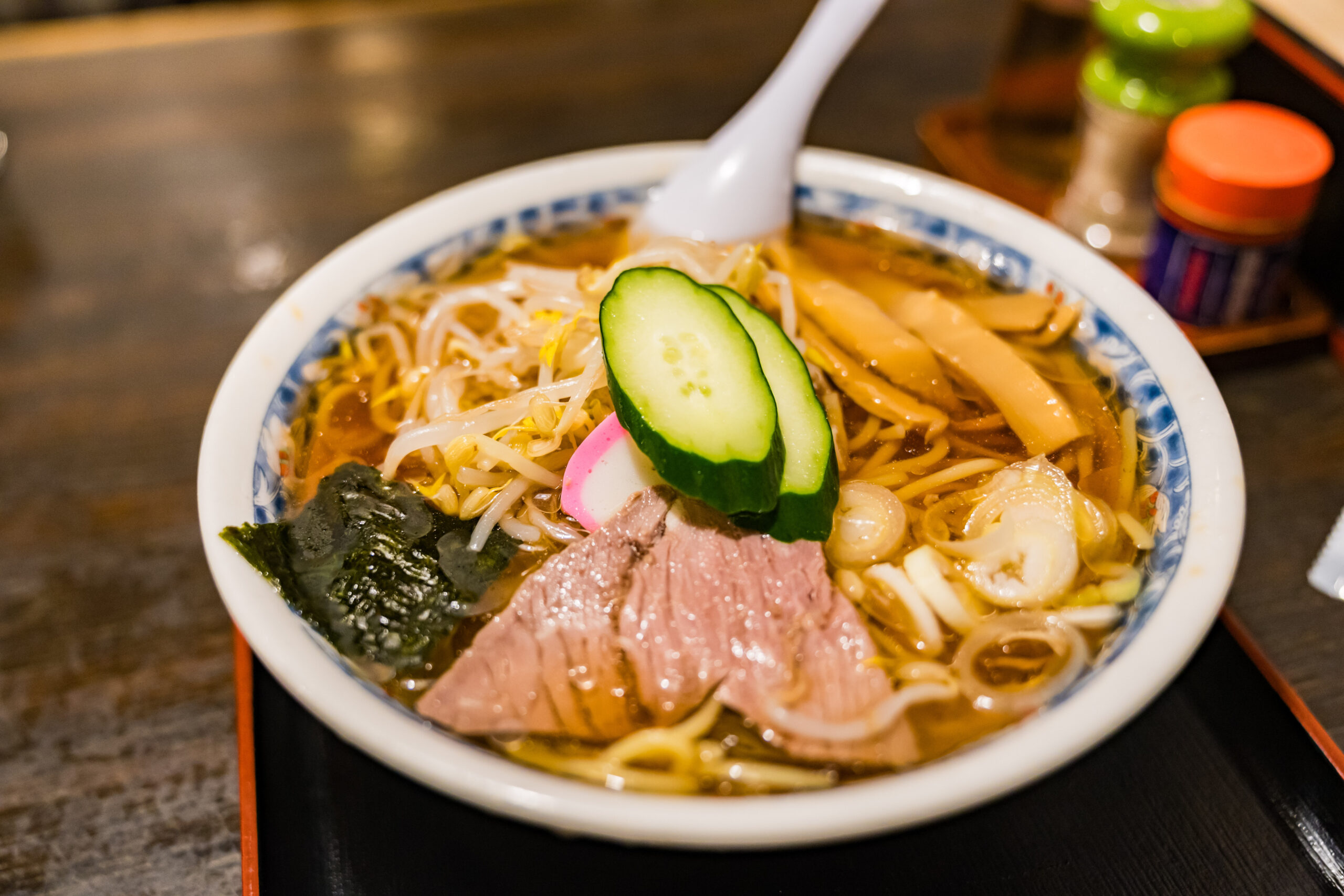 Bowl of ramen topped with cucumber slices, bean sprouts, pork, seaweed, and narutomaki in broth.