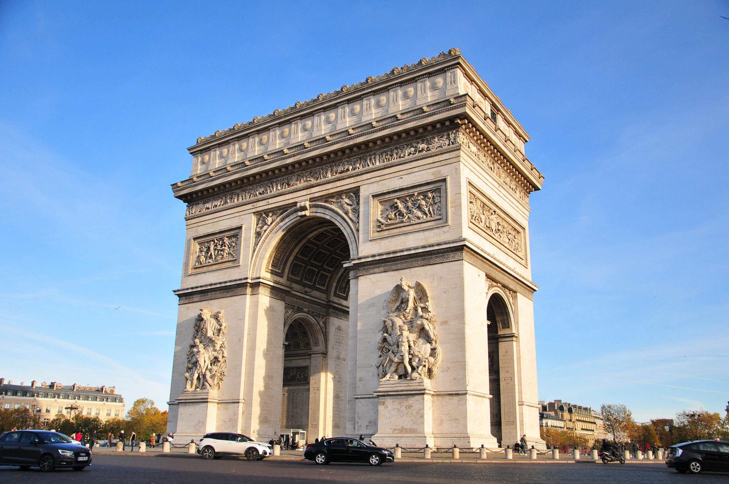 Arc de Triomphe monument in Paris under a clear blue sky, with detailed sculptures on its facade and arches in view.