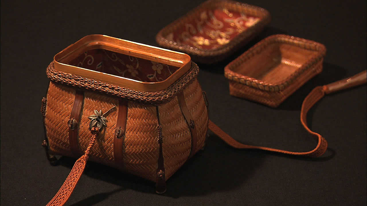 Three woven wicker handbags with leather straps and tassels, displayed on a dark surface; front bag is open to show red floral lining.